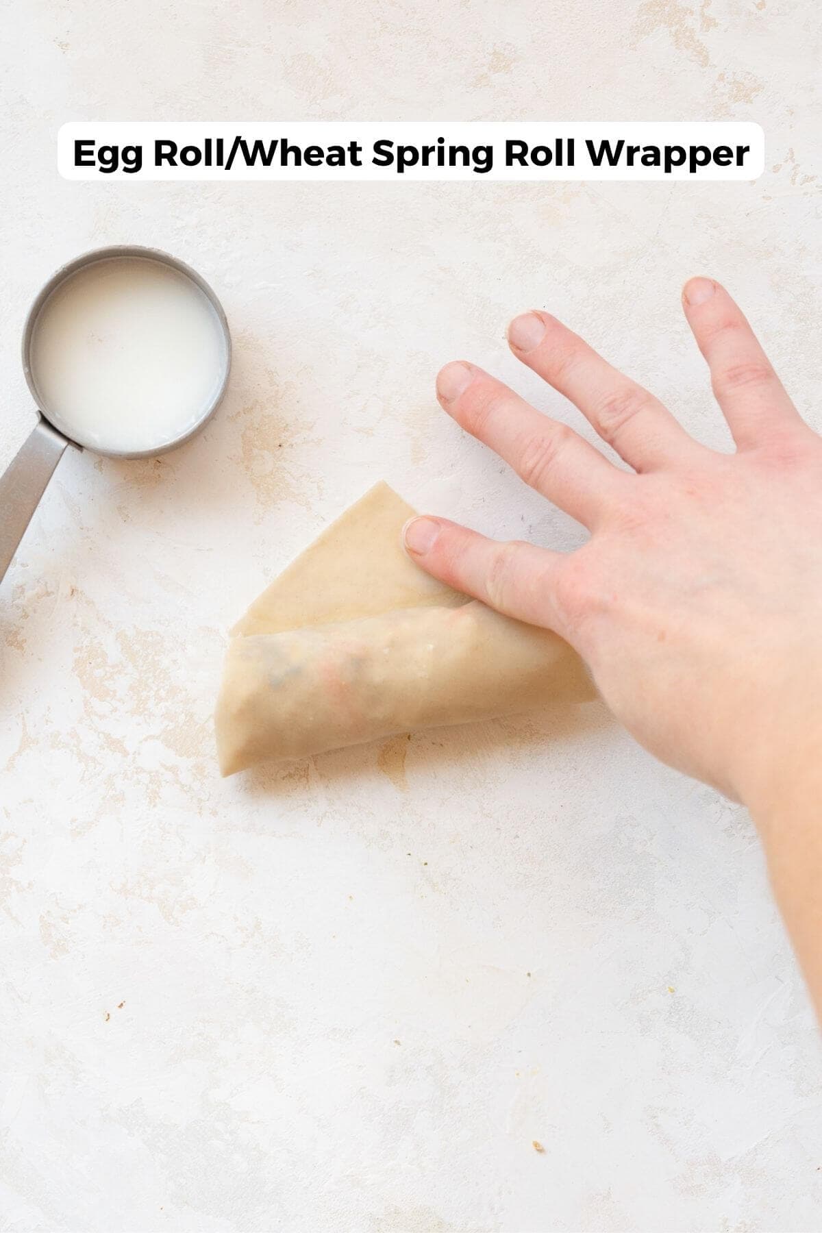 Hand rolling an egg roll wrapper around the spring roll filling.