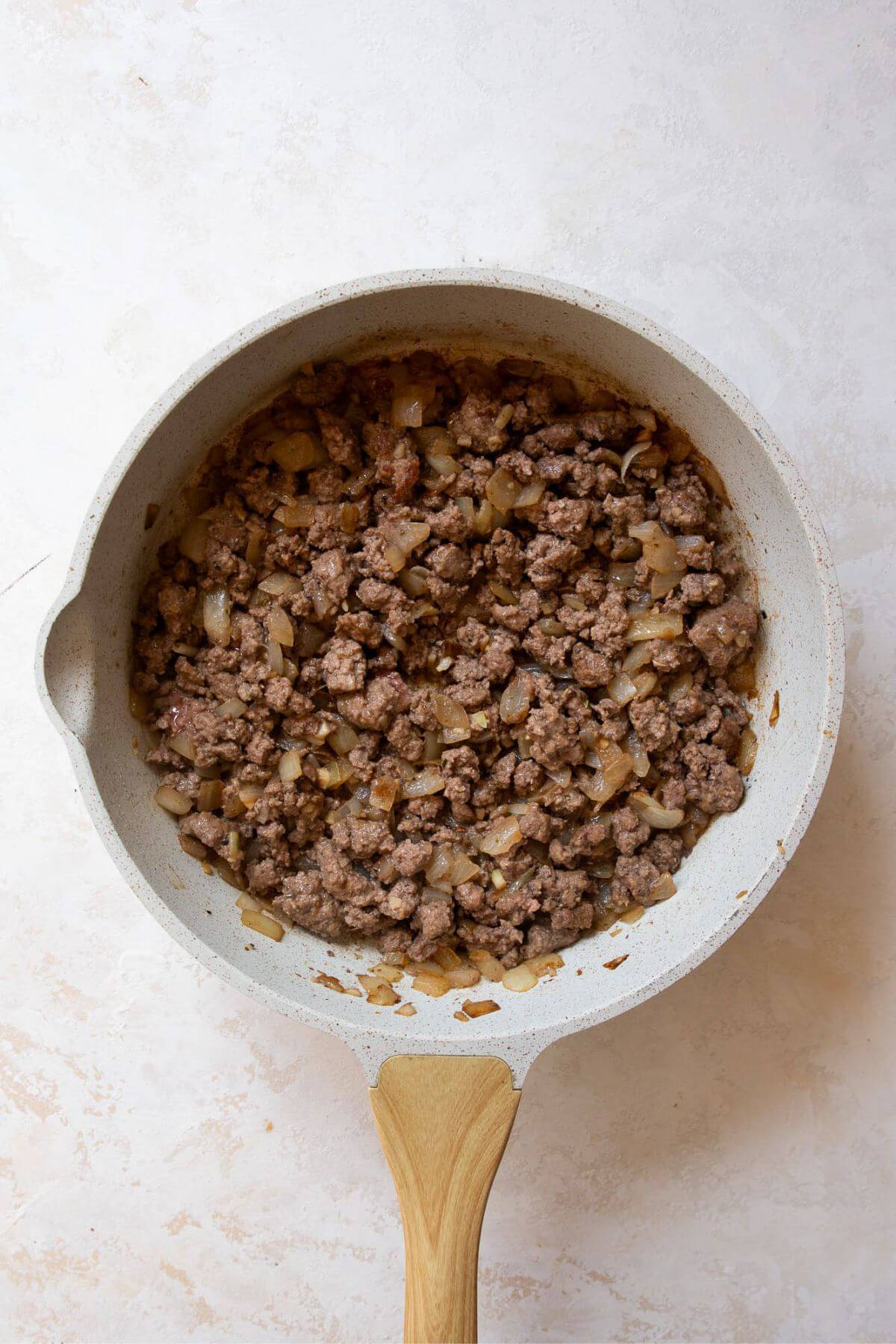 Ground beef browning in a skillet with sautéed onions and garlic.