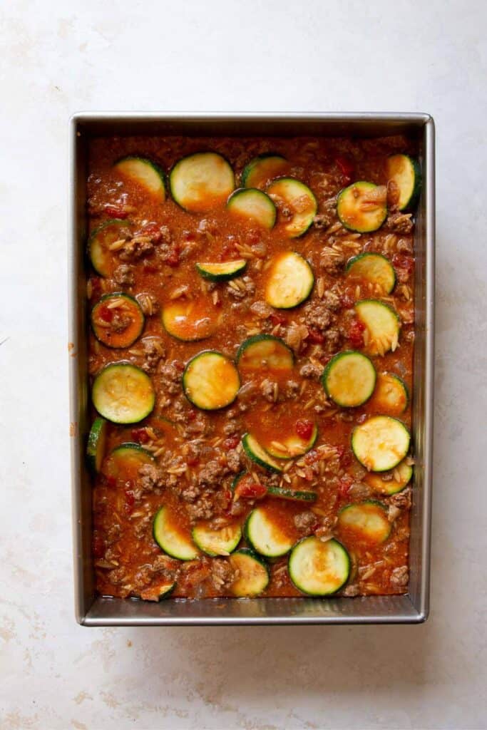 zucchini rounds and ground beef sauce in casserole dish before baking