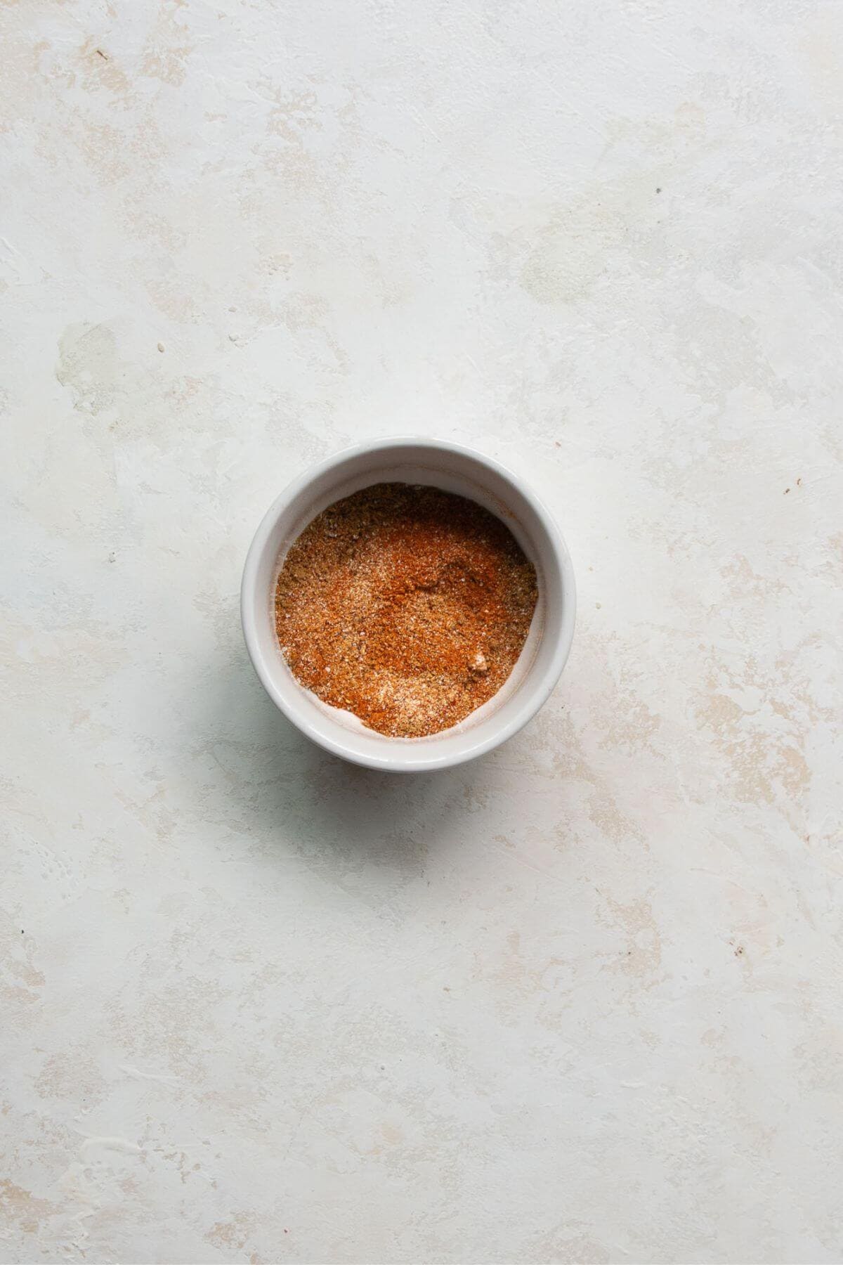 Fajita seasoning blend in a small white bowl on a marble counter.