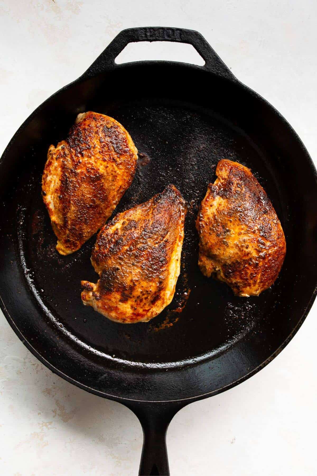 Searing three seasoned chicken breasts in a cast iron skillet.