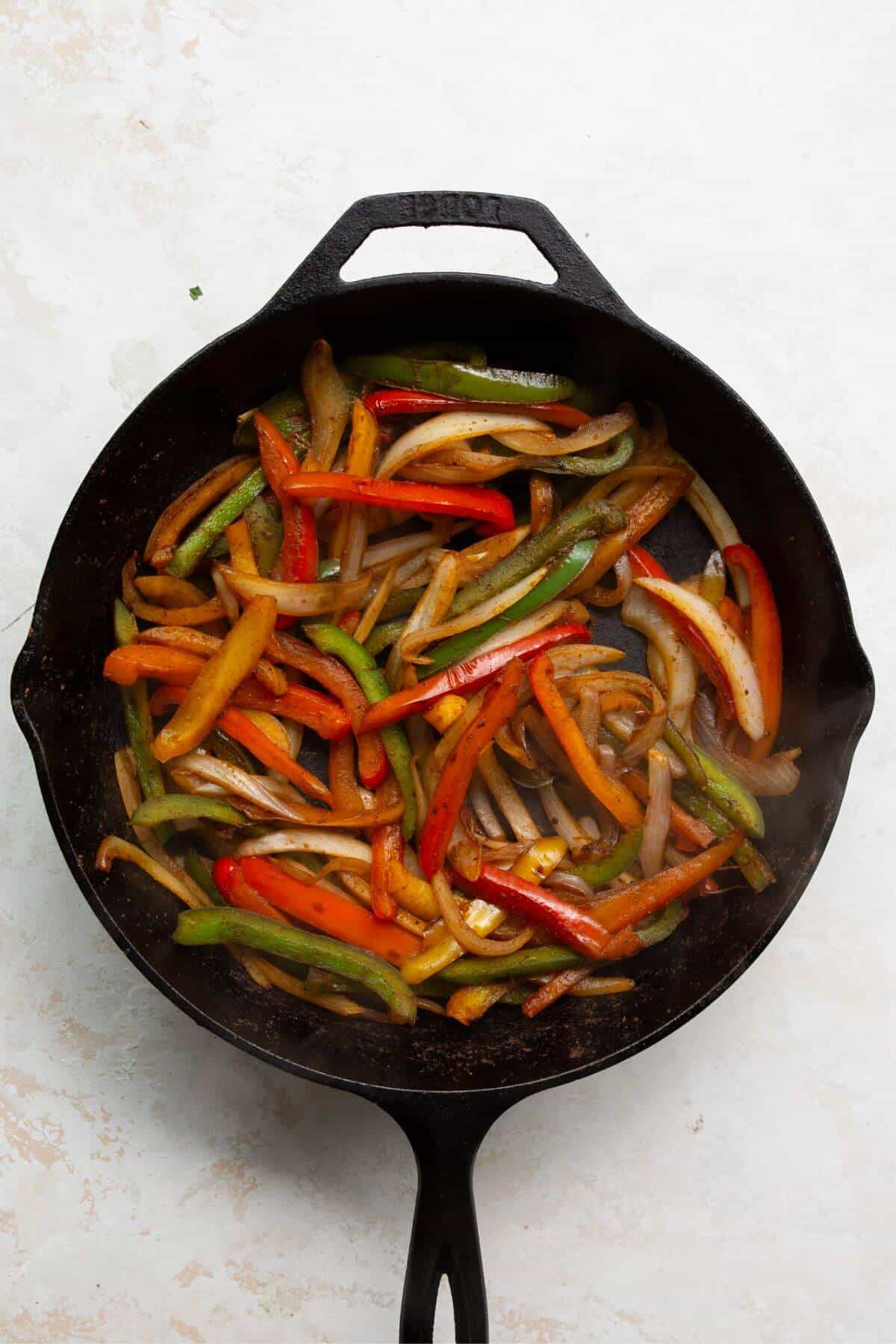 Sliced bell peppers and onions cooking in a cast iron skillet.