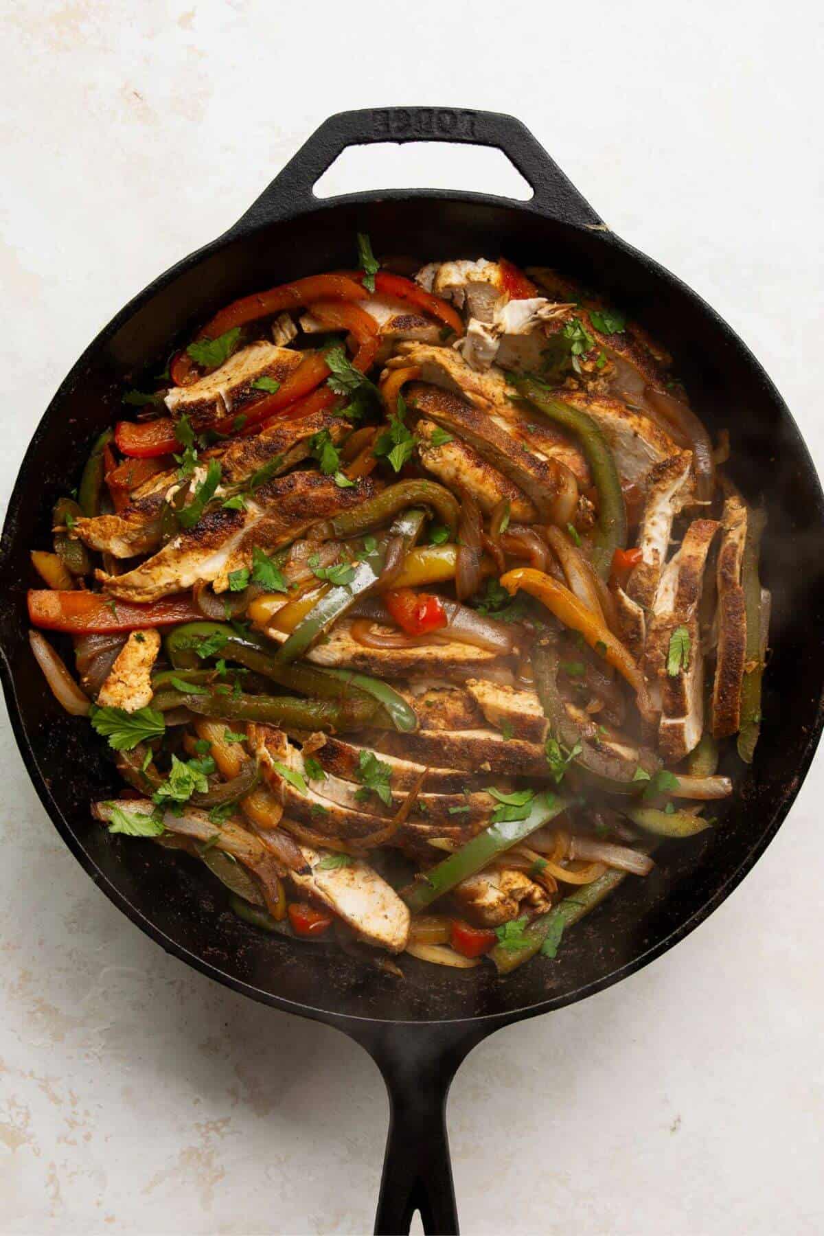 Finished chicken fajita filling with sliced chicken, peppers, and cilantro in a skillet.