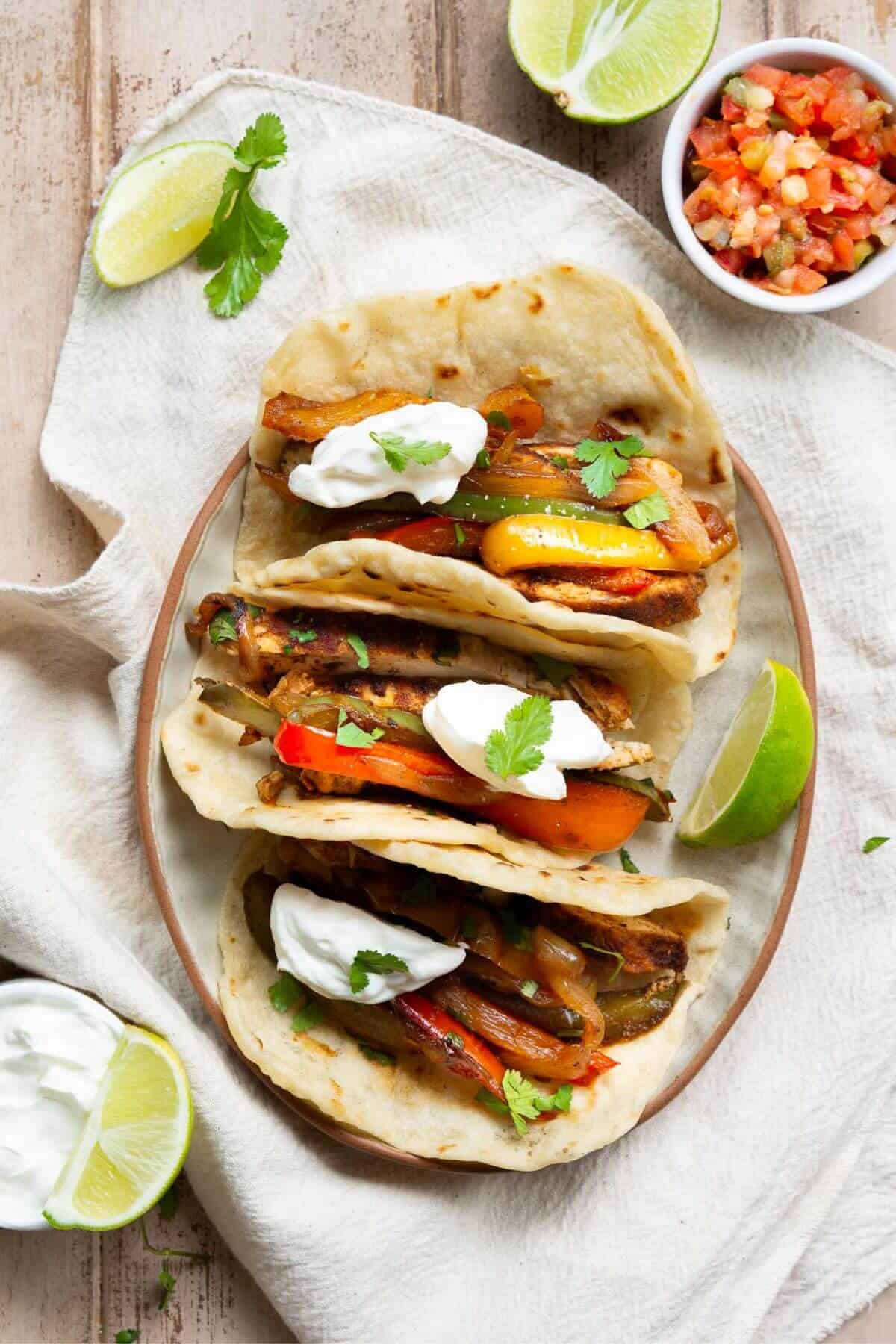 Healthy chicken fajita tacos on flour tortillas topped with cilantro, peppers, Greek yogurt, and lime.
