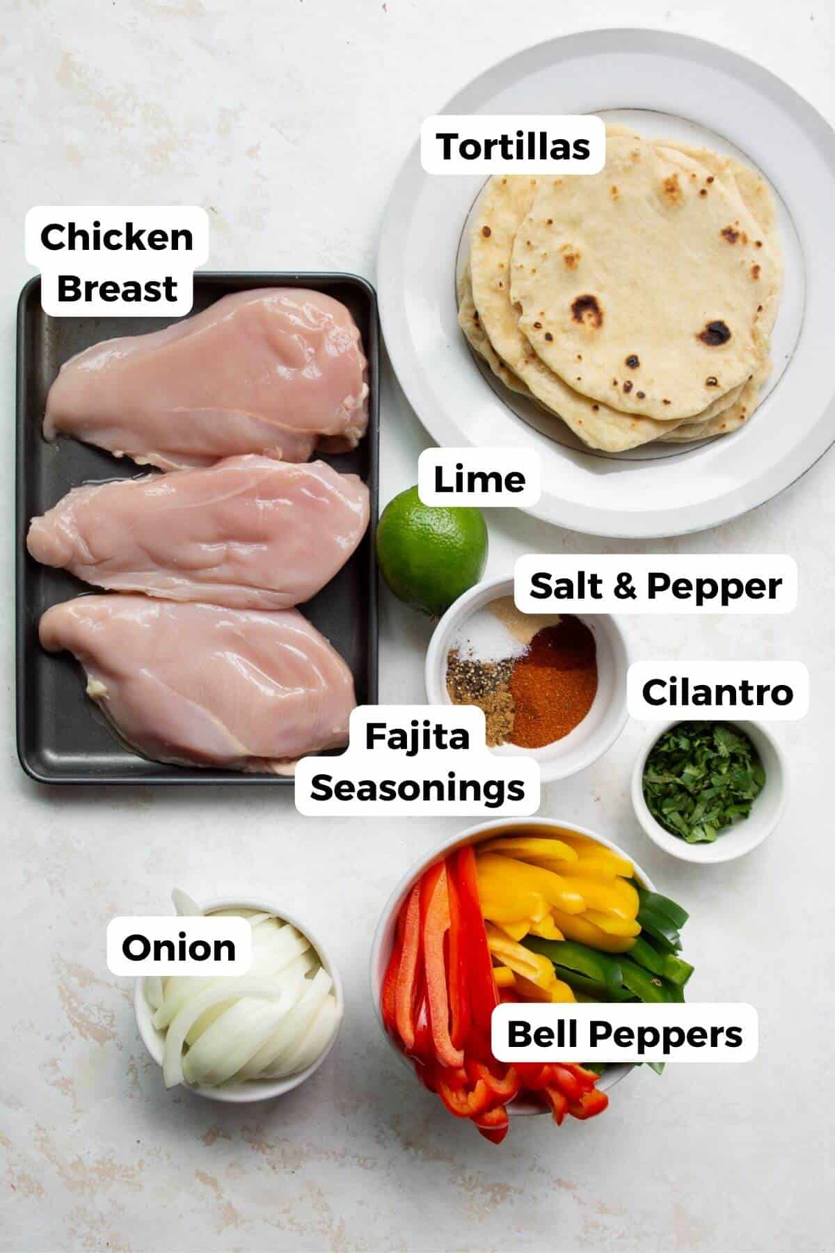 Ingredients for chicken fajita tacos:, including: raw chicken breasts, bell peppers, onion, lime, fajita seasonings, and tortillas.