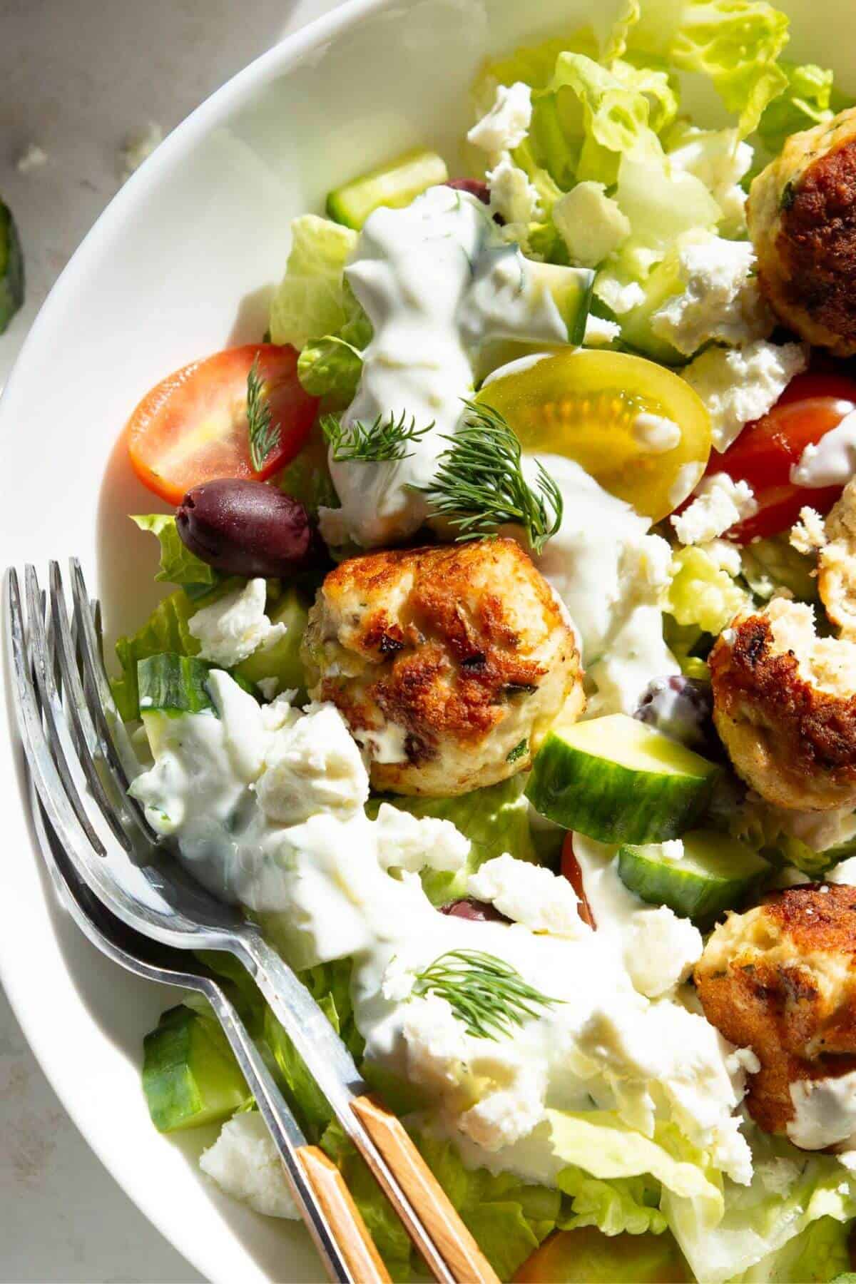 Greek chicken meatballs on a Greek salad with tzatziki and crumbled feta, garnished with fresh dill.