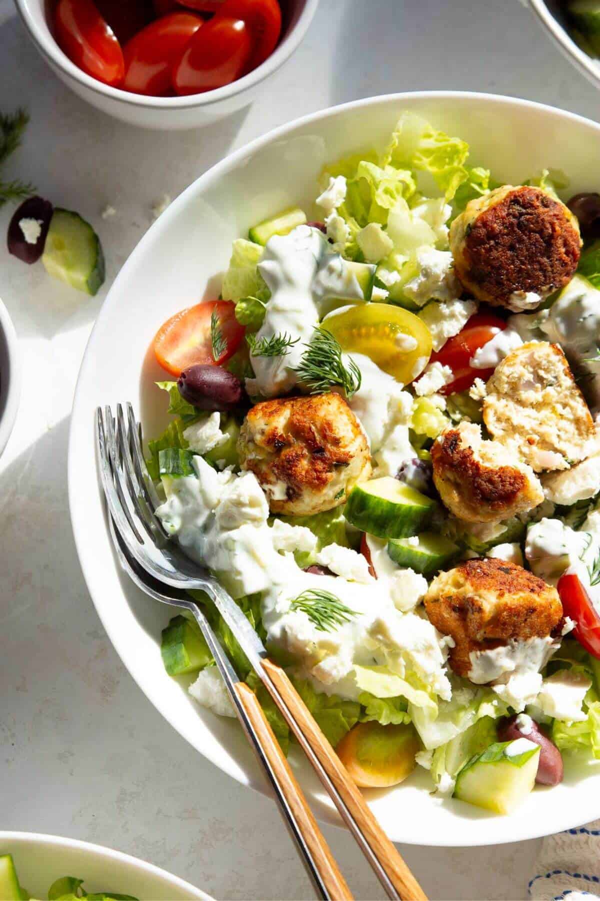 Healthy Greek chicken meatballs on a Greek salad with tzatziki, feta, cherry tomatoes, and cucumber in a bowl.