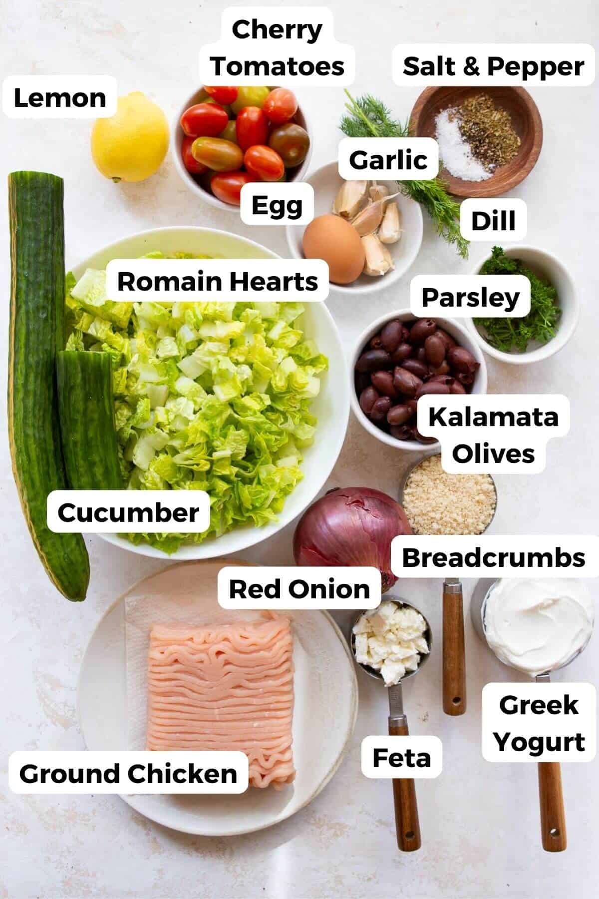 Ingredients for Greek chicken meatballs and tzatziki: ground chicken, egg, panko breadcrumbs, red onion, garlic, parsley, dill, romaine, cucumber, cherry tomatoes, kalamata olives, feta, Greek yogurt, and lemon..