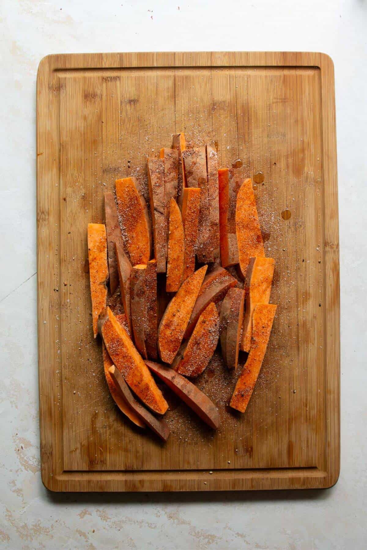 Olive oil and seasoning drizzle on cut up sweet potato wedges.