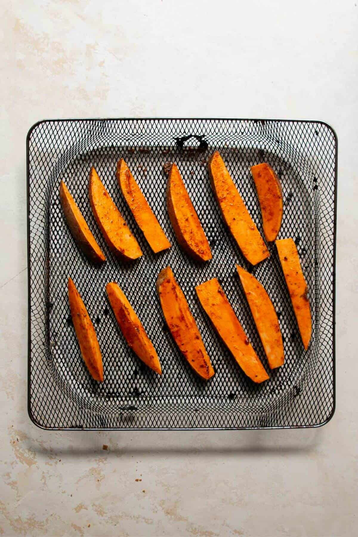 Raw sweet potato wedges in air fryer basket.