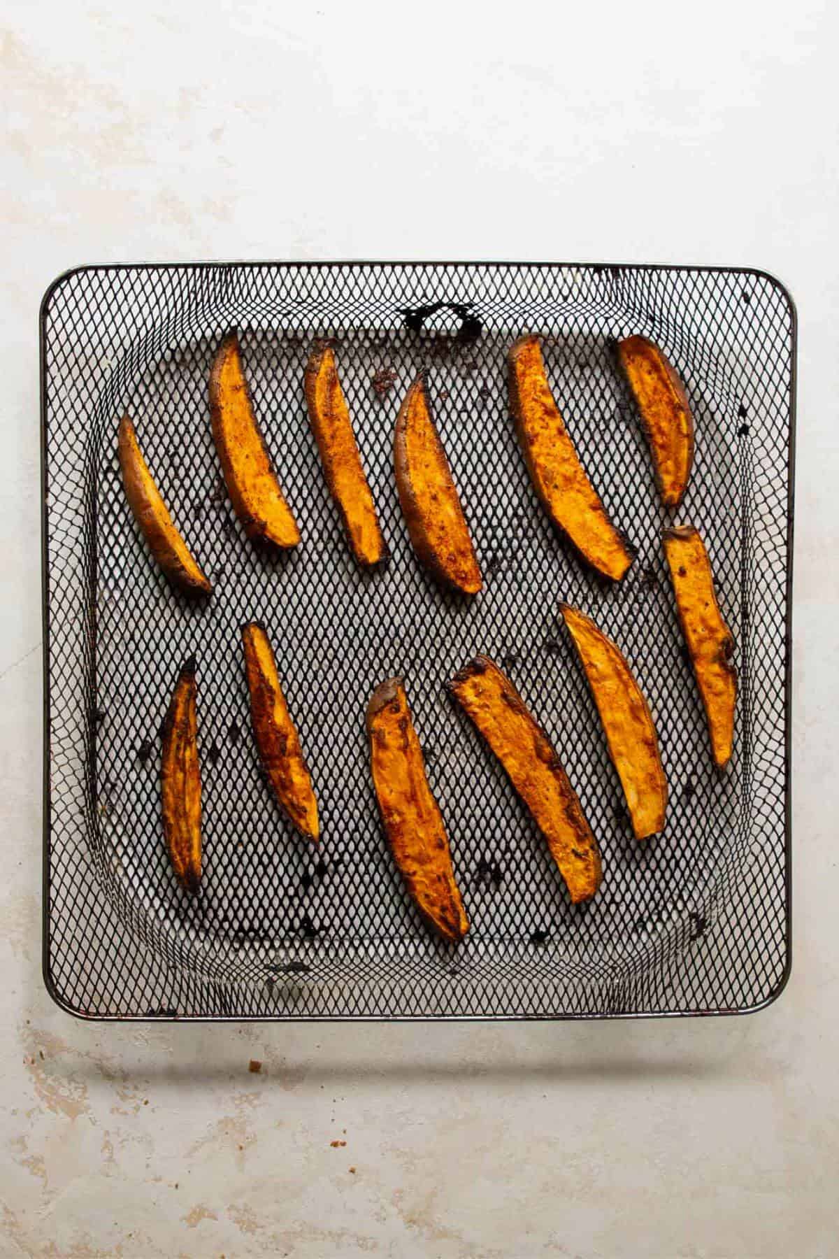 Cooked crispy air fryer sweet potato wedges in an air fryer basket.