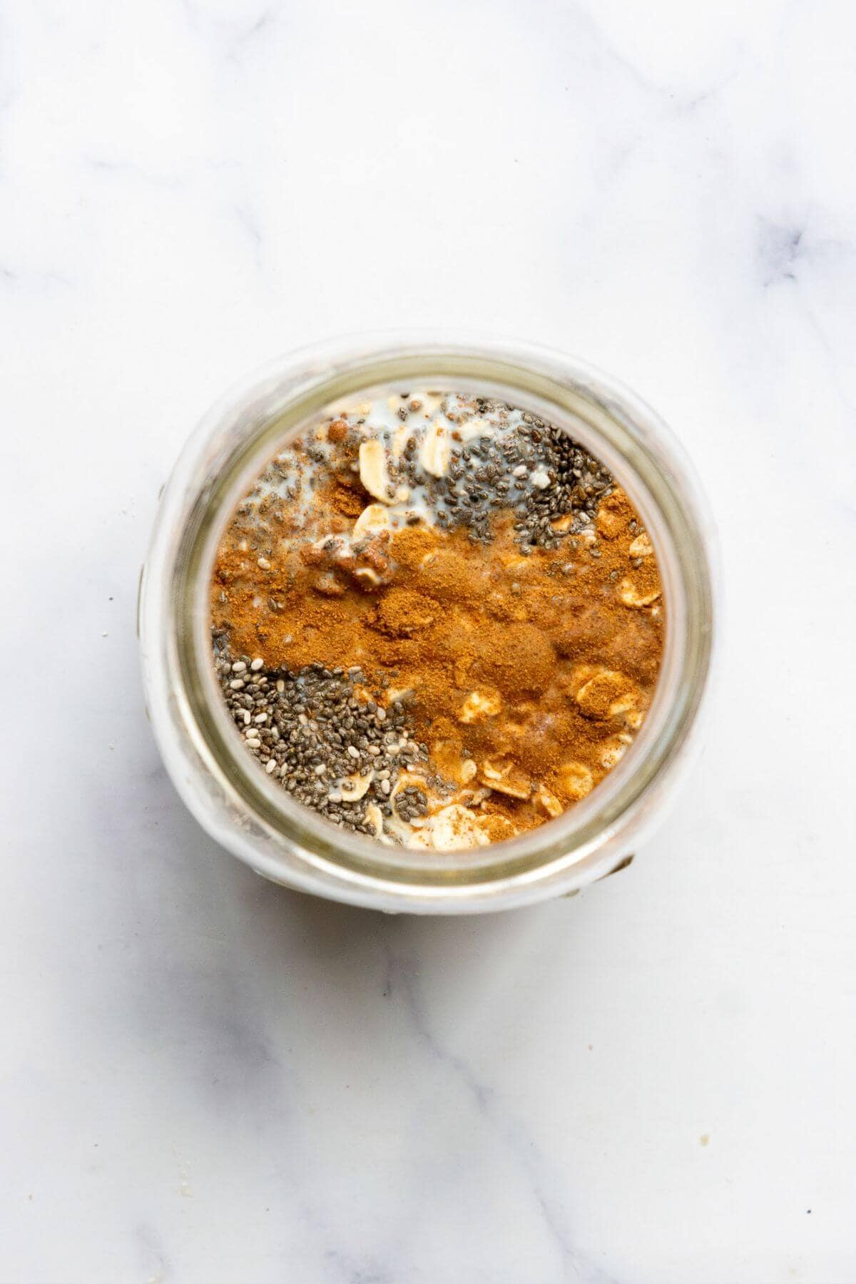 Cinnamon and chia seeds layered over oats and milk in a glass jar.