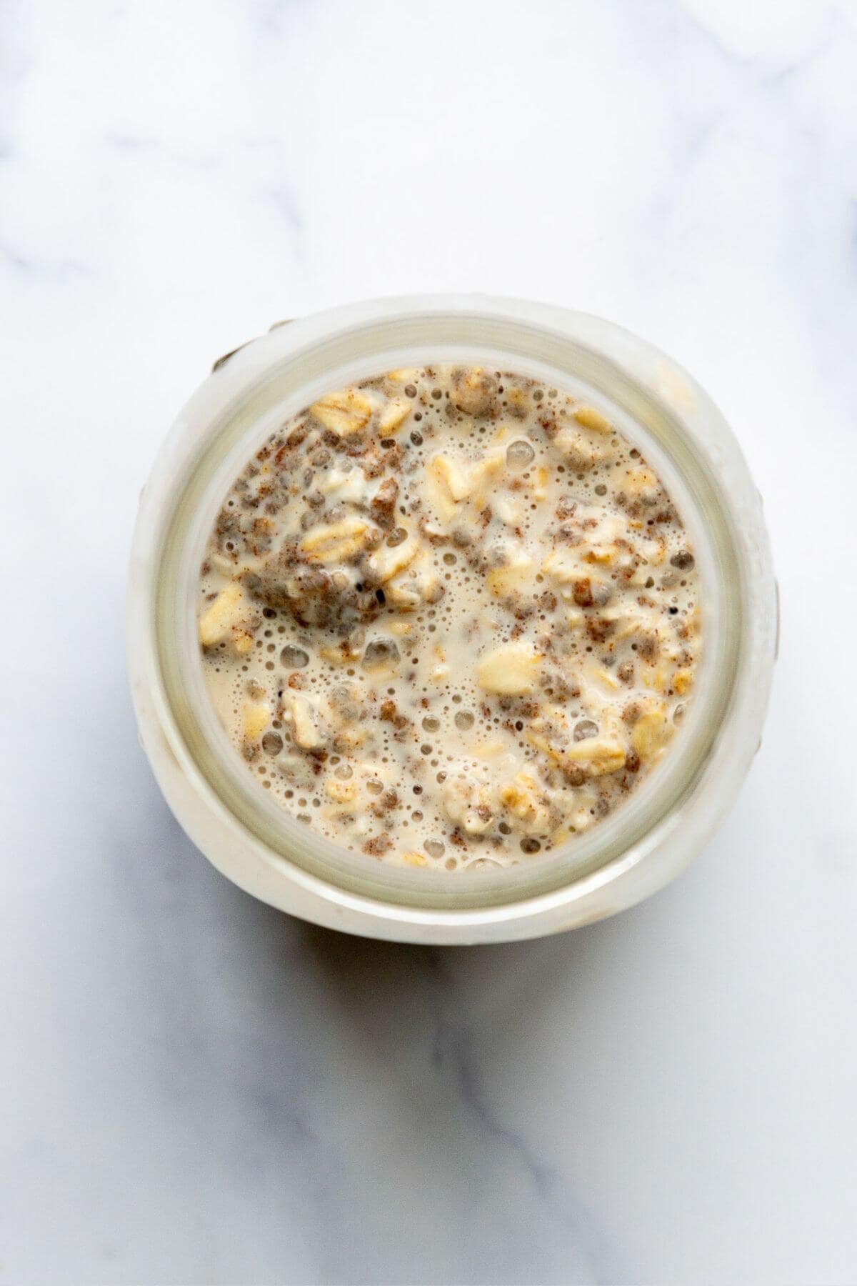 Cinnamon overnight oats stirred together in a glass jar before chilling.