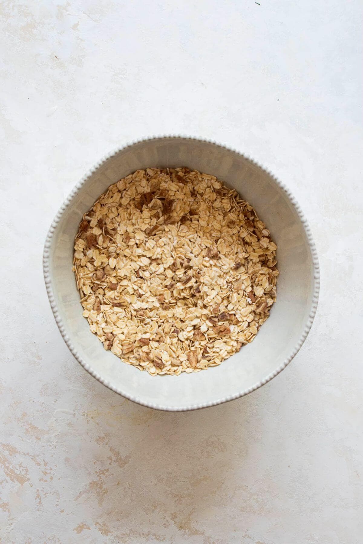 Rolled oats, chopped almonds, and pecans mixed in a white bowl before adding wet ingredients for homemade healthy granola.