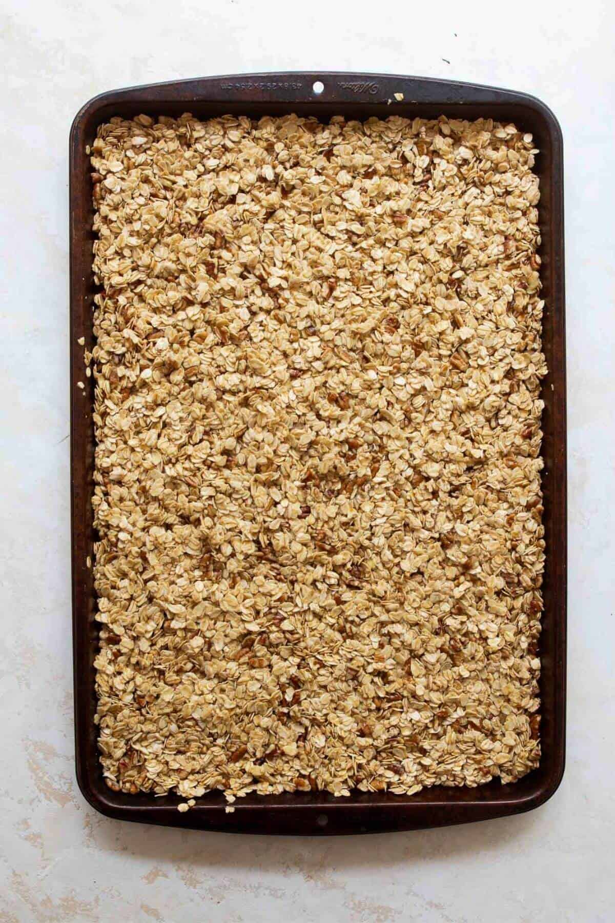 Homemade granola mixture pressed firmly into an even layer on a baking sheet, the key step for chunky clusters.