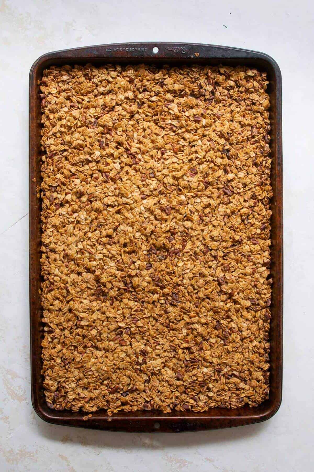 Golden-brown chunky healthy granola fresh out of the oven, cooling on the baking sheet to form clusters.