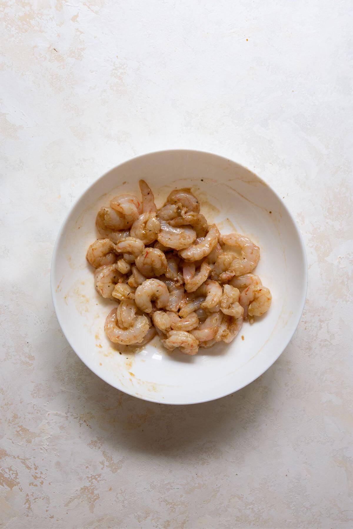 Raw shrimp tossed with garlic and balsamic dressing, marinating in a white bowl.