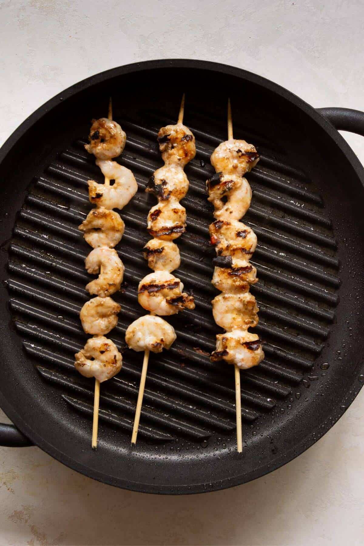 Shrimp threaded onto skewers and grilling on a cast iron grill pan.