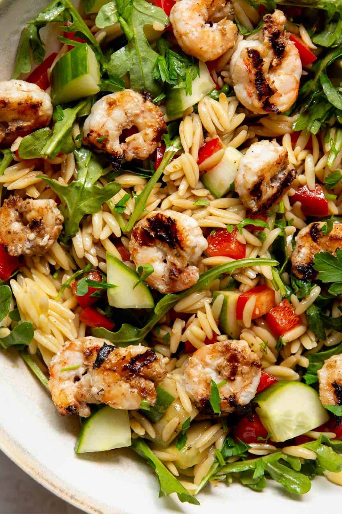 Close up grilled shrimp orzo salad showing charred shrimp, orzo, cucumber, and arugula.