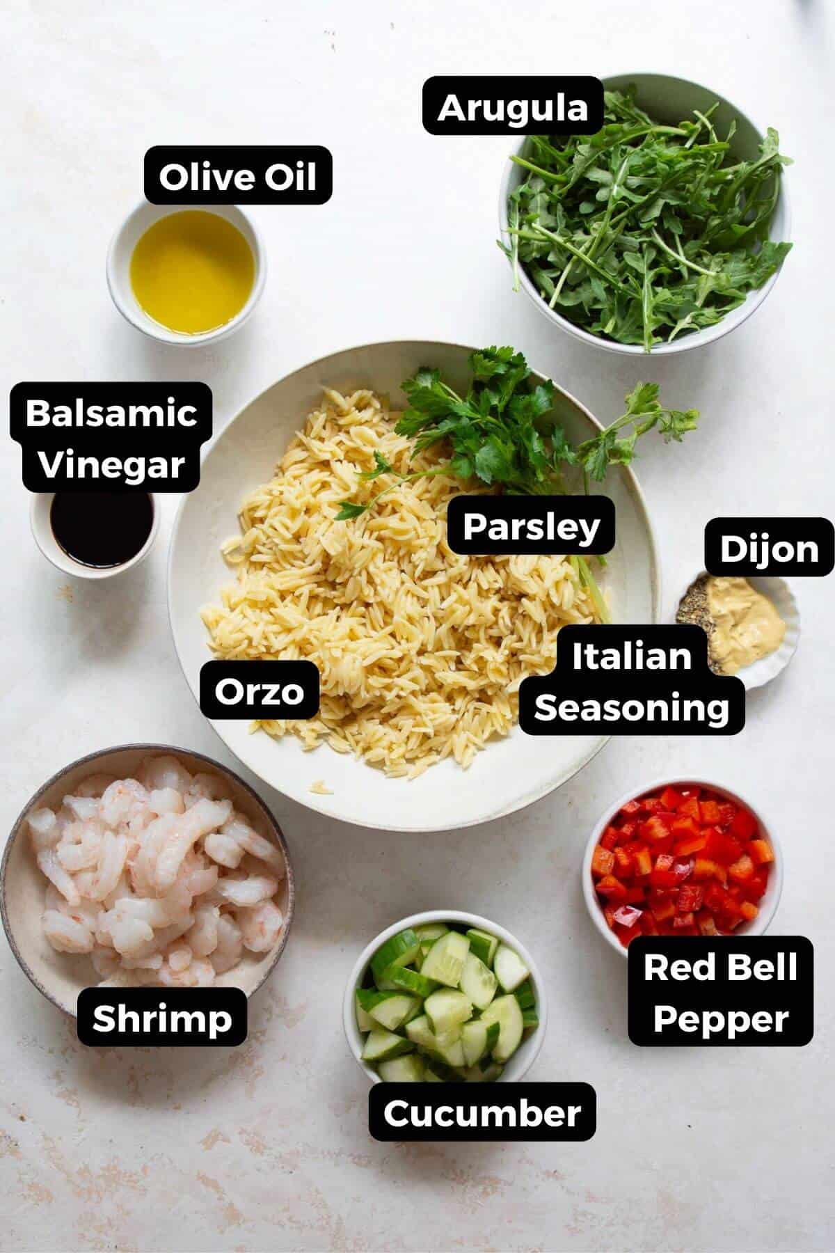 Ingredients for shrimp orzo salad laid out in bowls: shrimp, orzo, arugula, cucumber, red bell pepper, parsley, olive oil, balsamic vinegar, and Dijon.