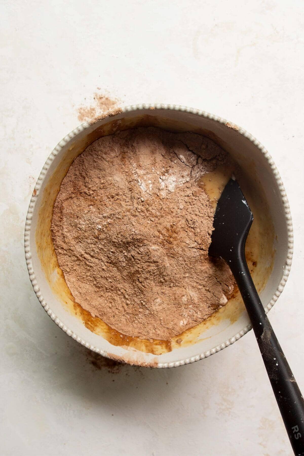Cocoa powder and flour added on top of wet muffin batter in a mixing bowl.