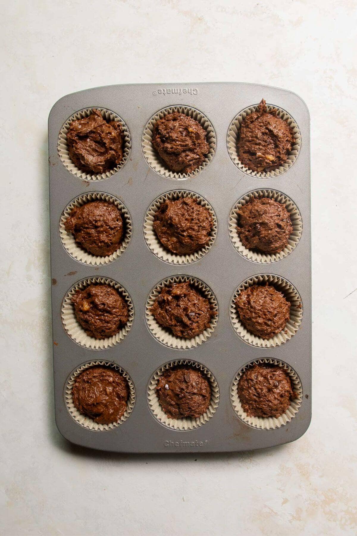 Unbaked chocolate banana muffin batter scooped into a 12-cup muffin tin.