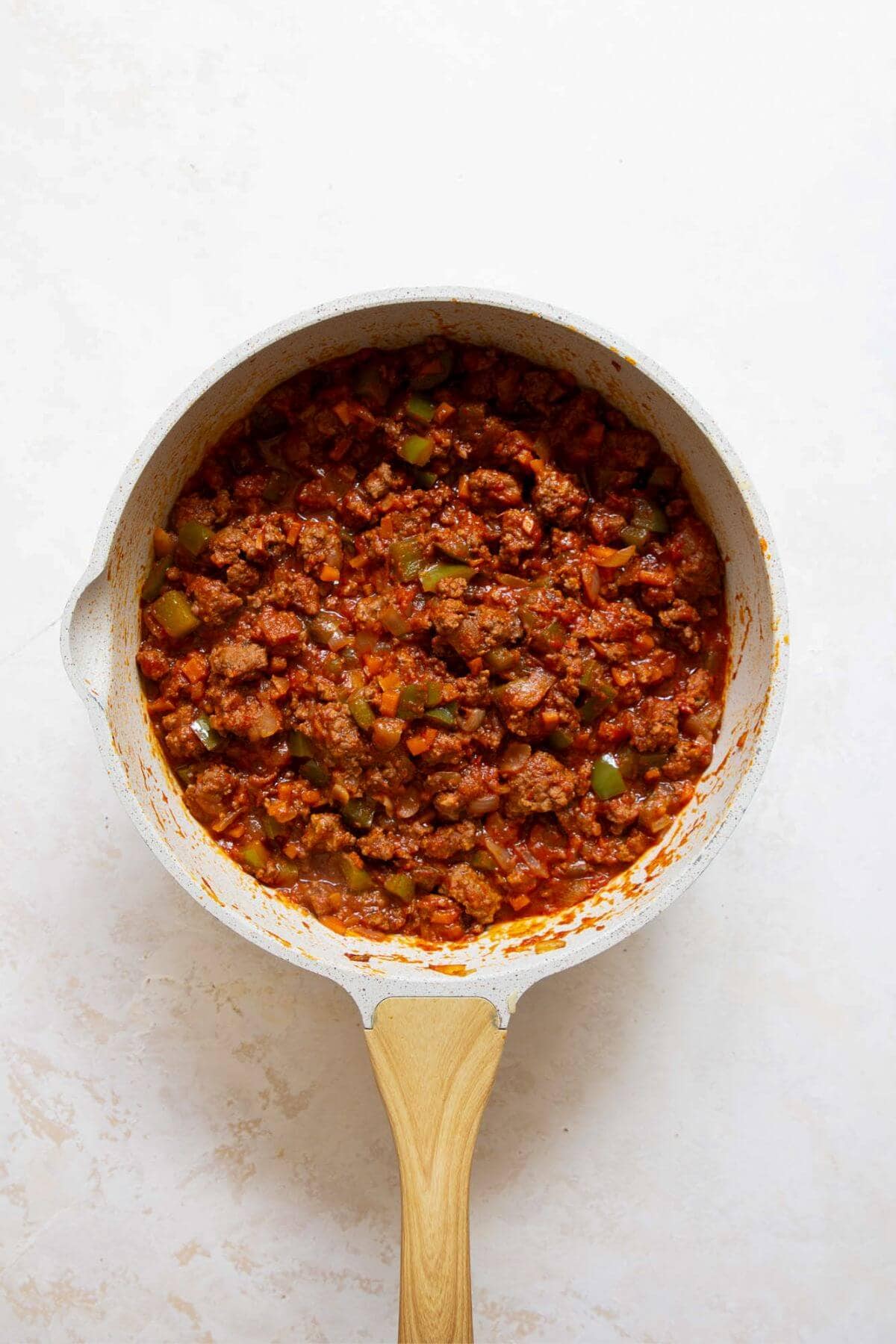 Adding tomato paste, crushed tomatoes, and seasonings into the browned beef mixture before simmering.