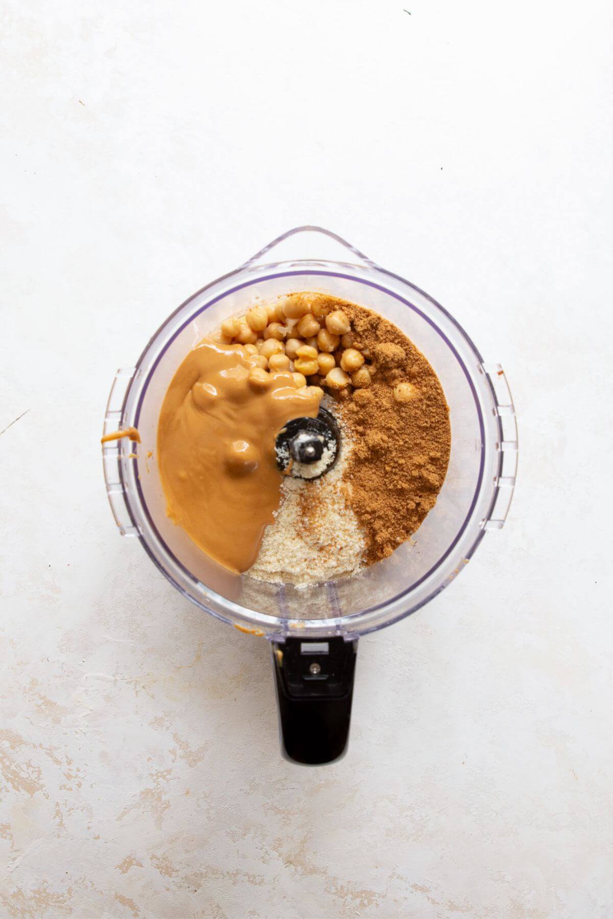 Chickpeas, peanut butter, maple syrup, and almond flour in a food processor before blending.
