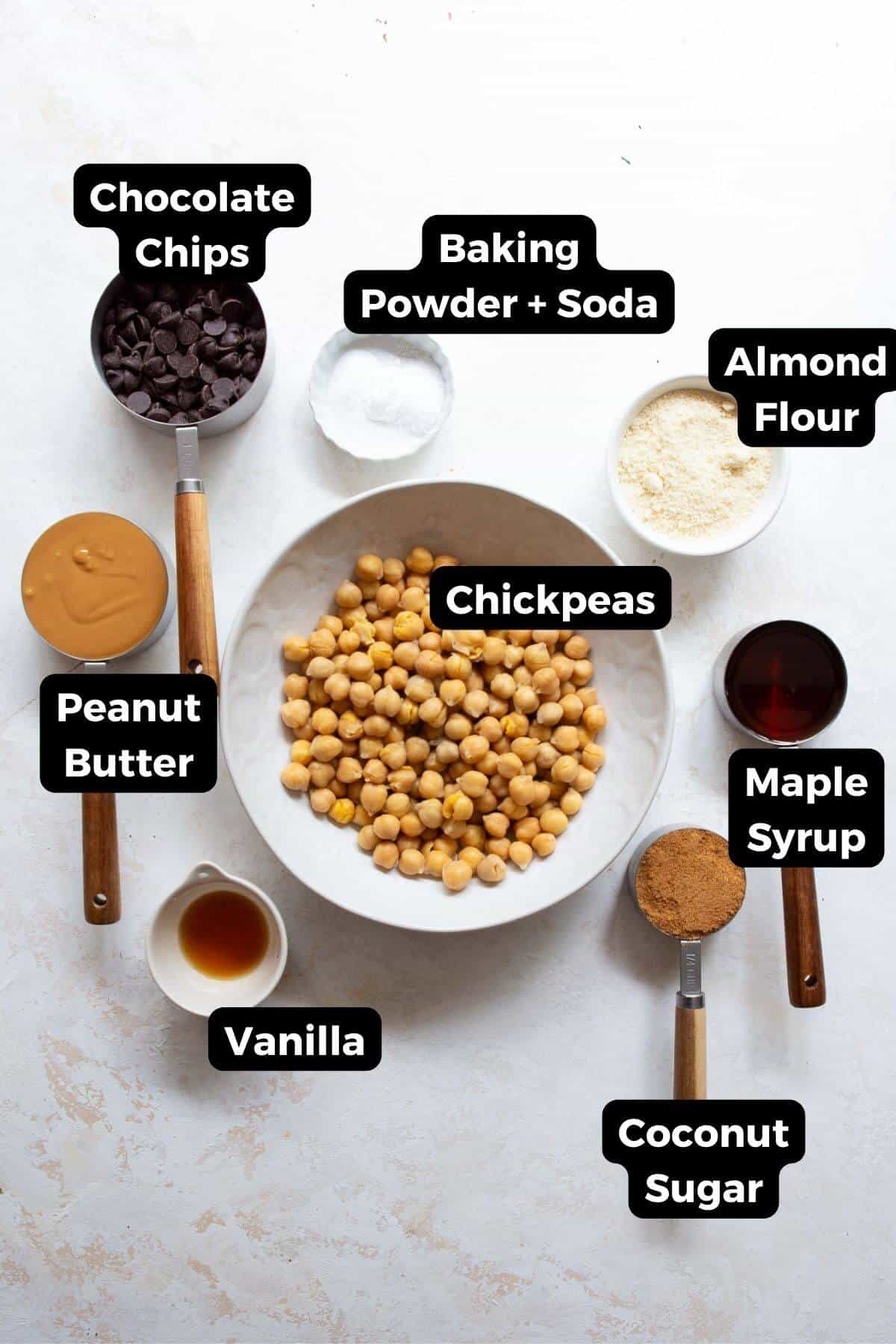 Ingredients for chickpea blondies, including chickpeas, peanut butter, almond flour, maple syrup, coconut sugar, vanilla, baking powder, baking soda, and chocolate chips.