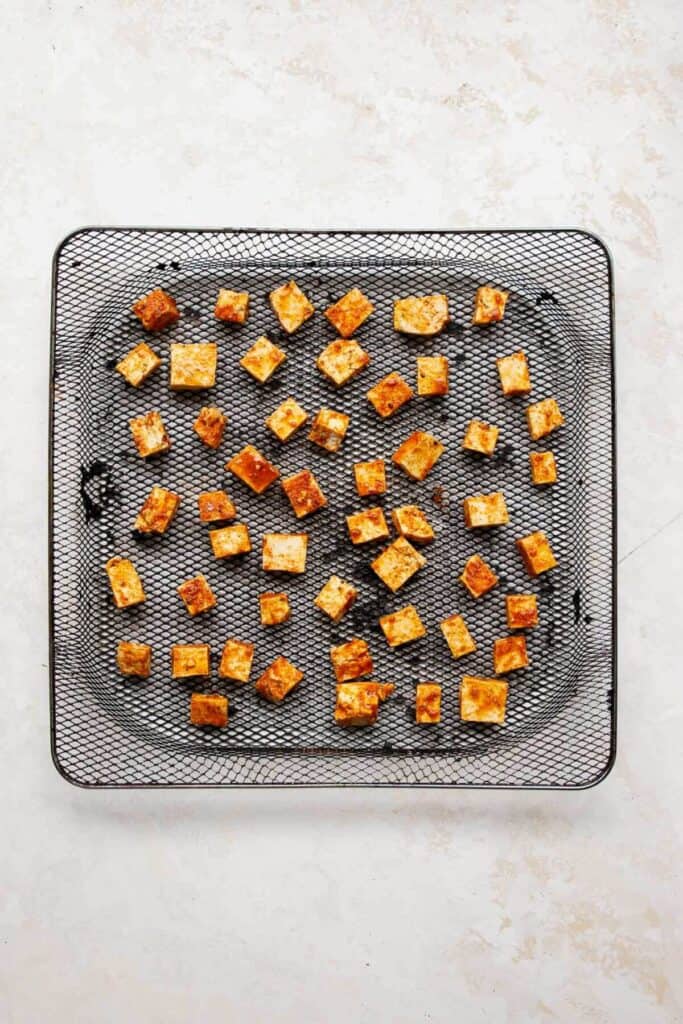 raw seasoned tofu cubes in an air fryer basket