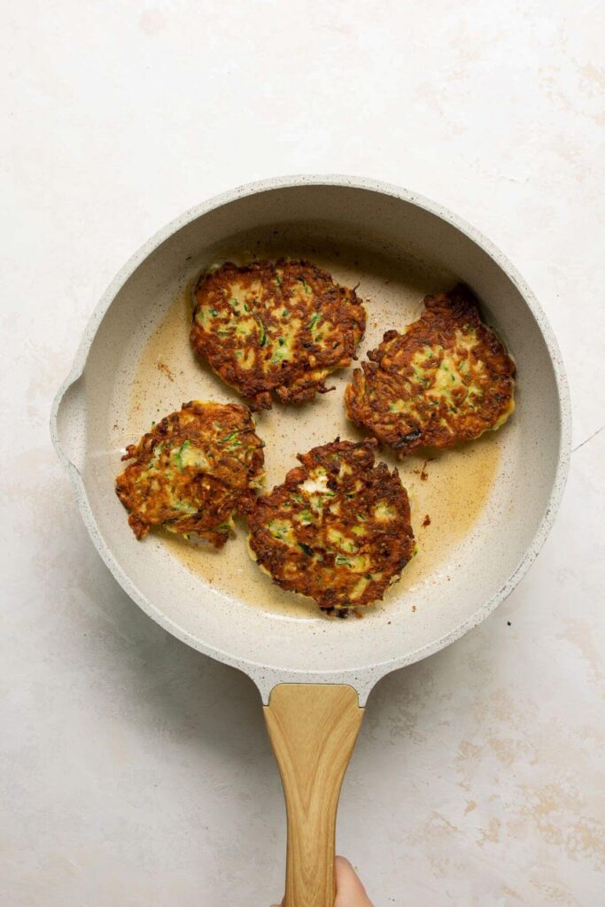 golden crispy zucchini fritters in a pan after flipping