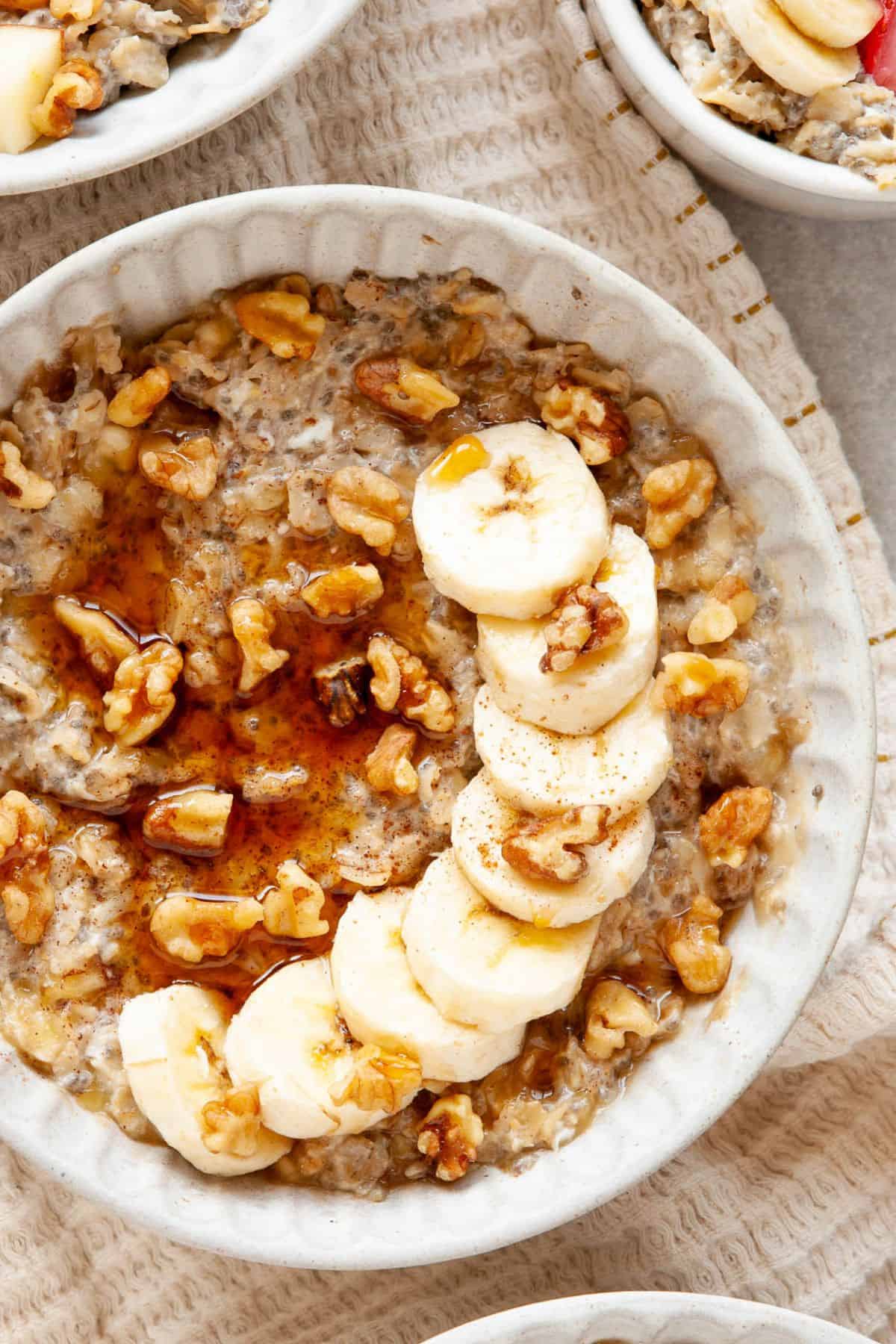A bowl of creamy egg white oatmeal with banana slices, walnuts, and a drizzle of maple syrup.