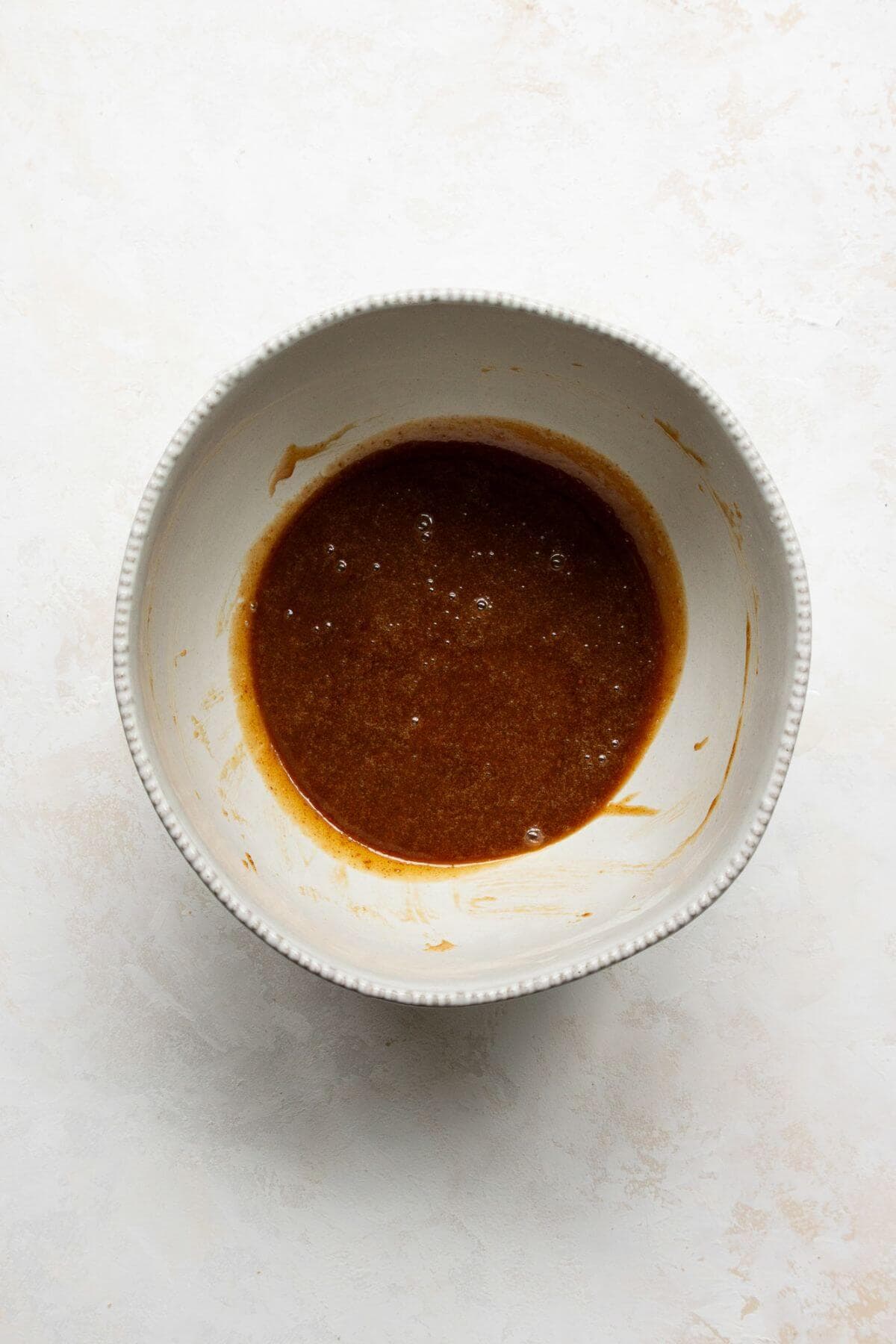 Whisked eggs, coconut sugar, vanilla, and coconut oil mixed in a bowl.