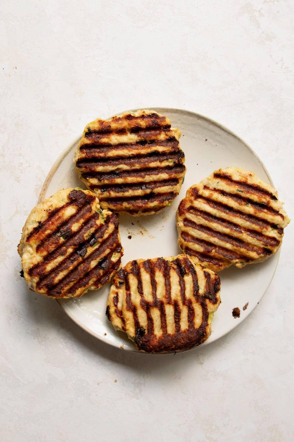 Four grilled, cooked, juicy chicken burgers on a plate.