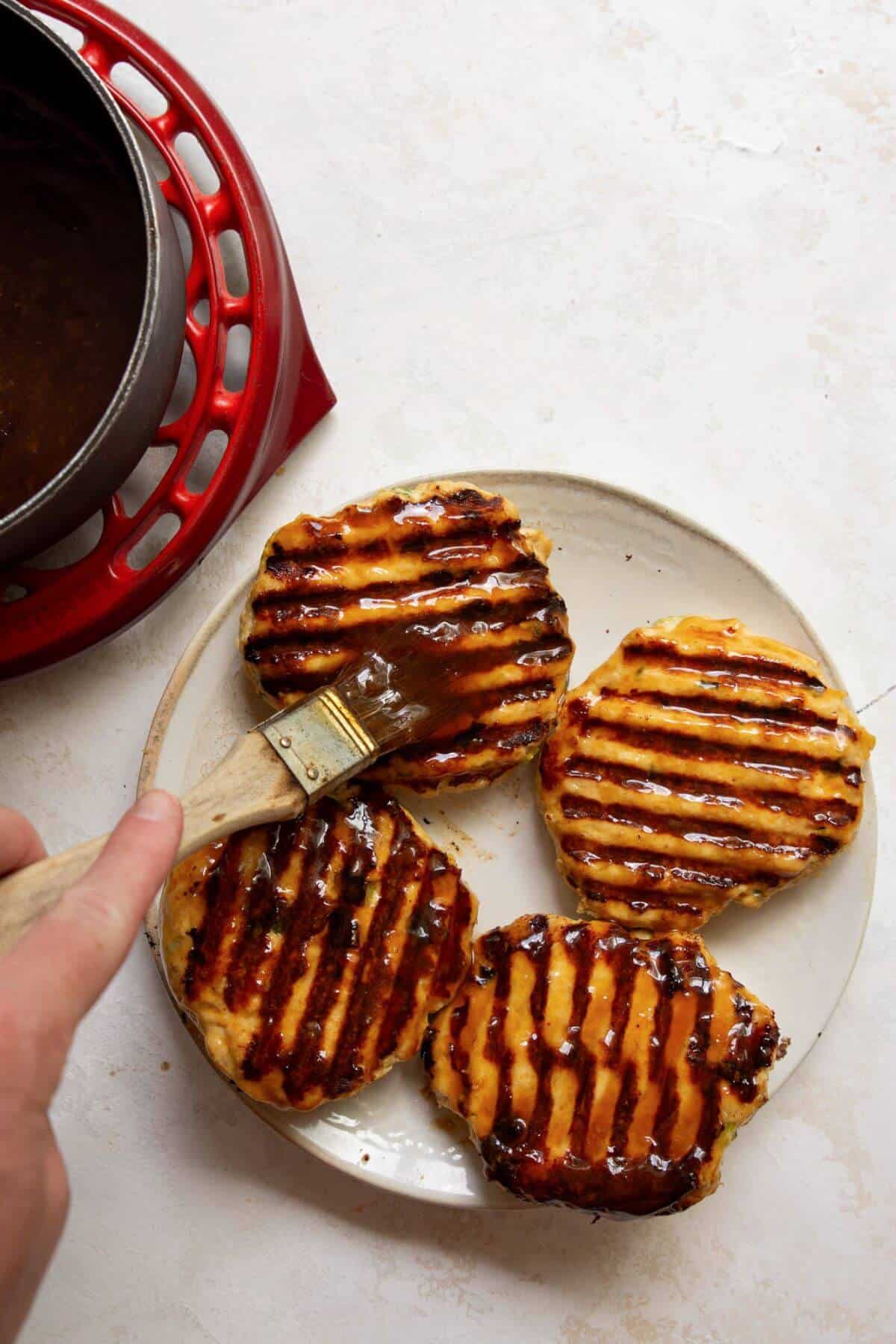 Brushing teriyaki sauce onto cooked chicken burgers.
