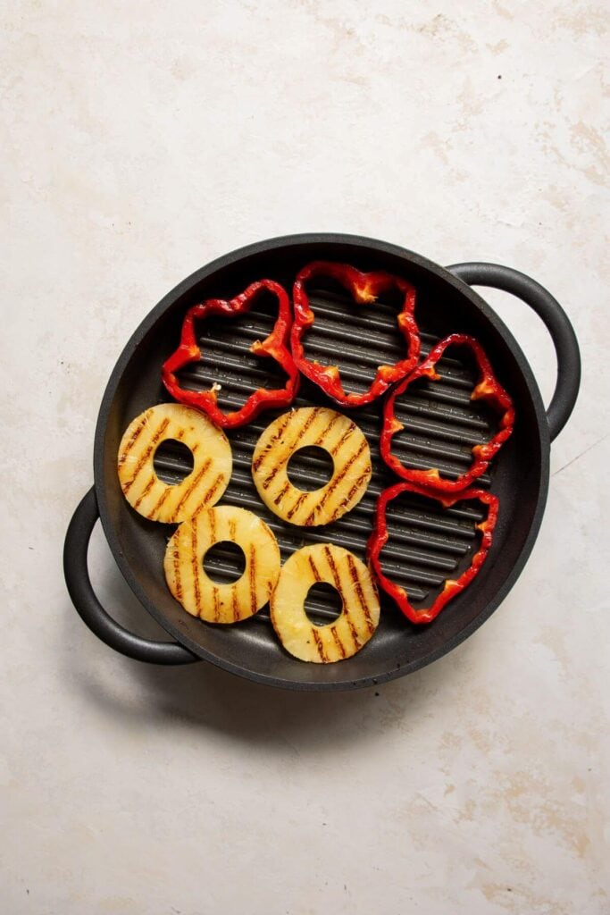 grilling pineapple and red bell pepper rings on a grill pan