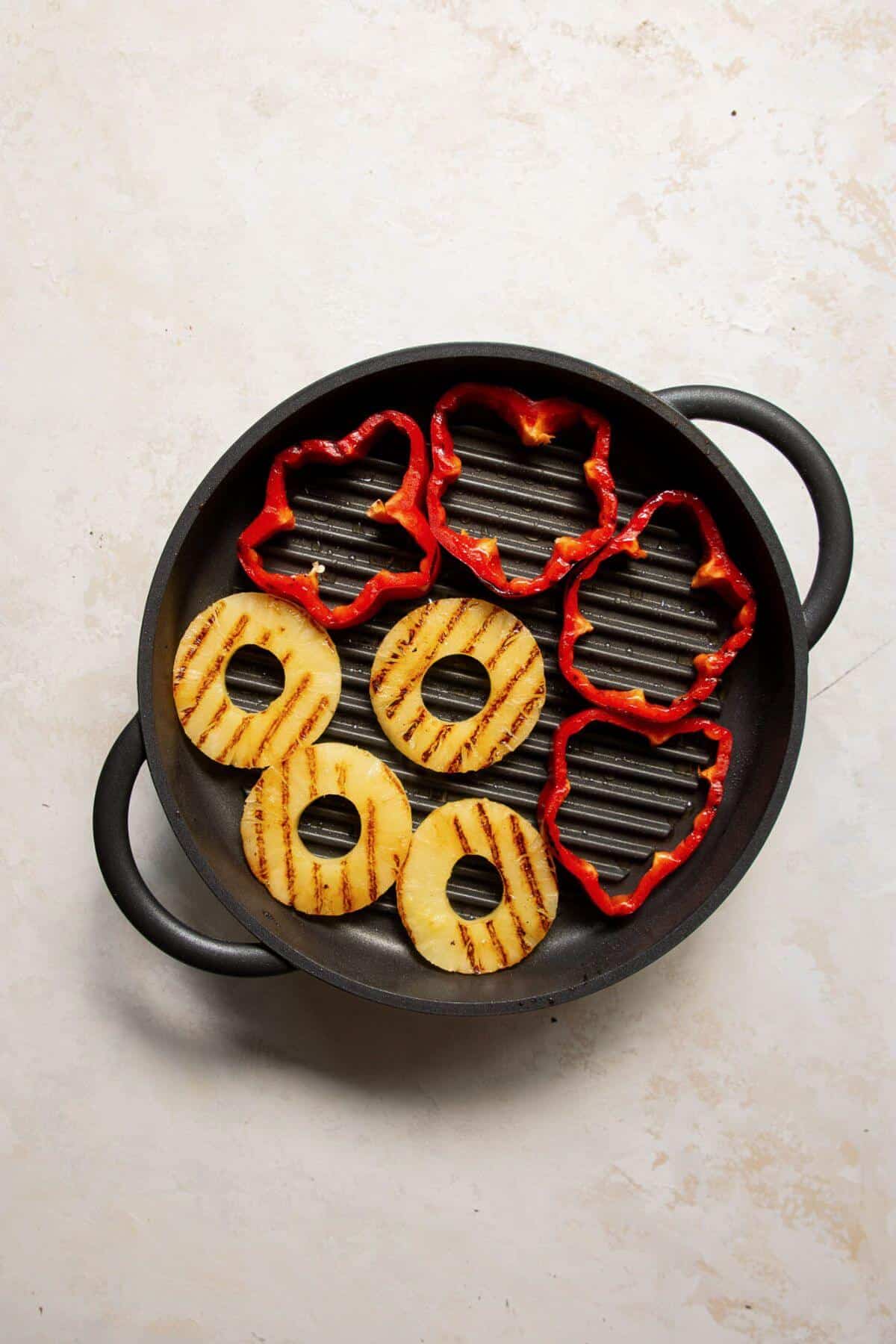 Grilled pineapple rings and red bell pepper slices caramelizing on grill.