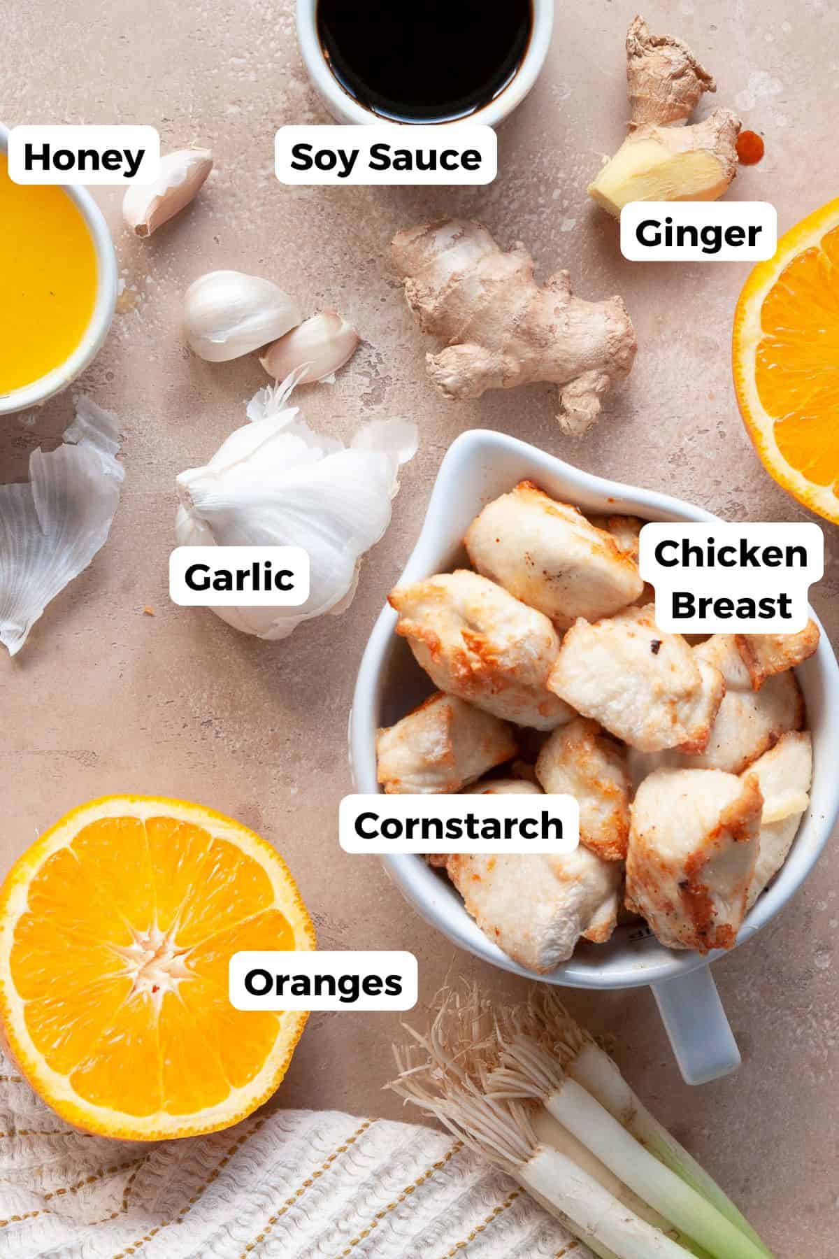 All ingredients in small labeled bowls, including chicken breast, soy sauce, orange juice, sesame oil, honey, vinegar, garlic, ginger, and arrowroot starch.