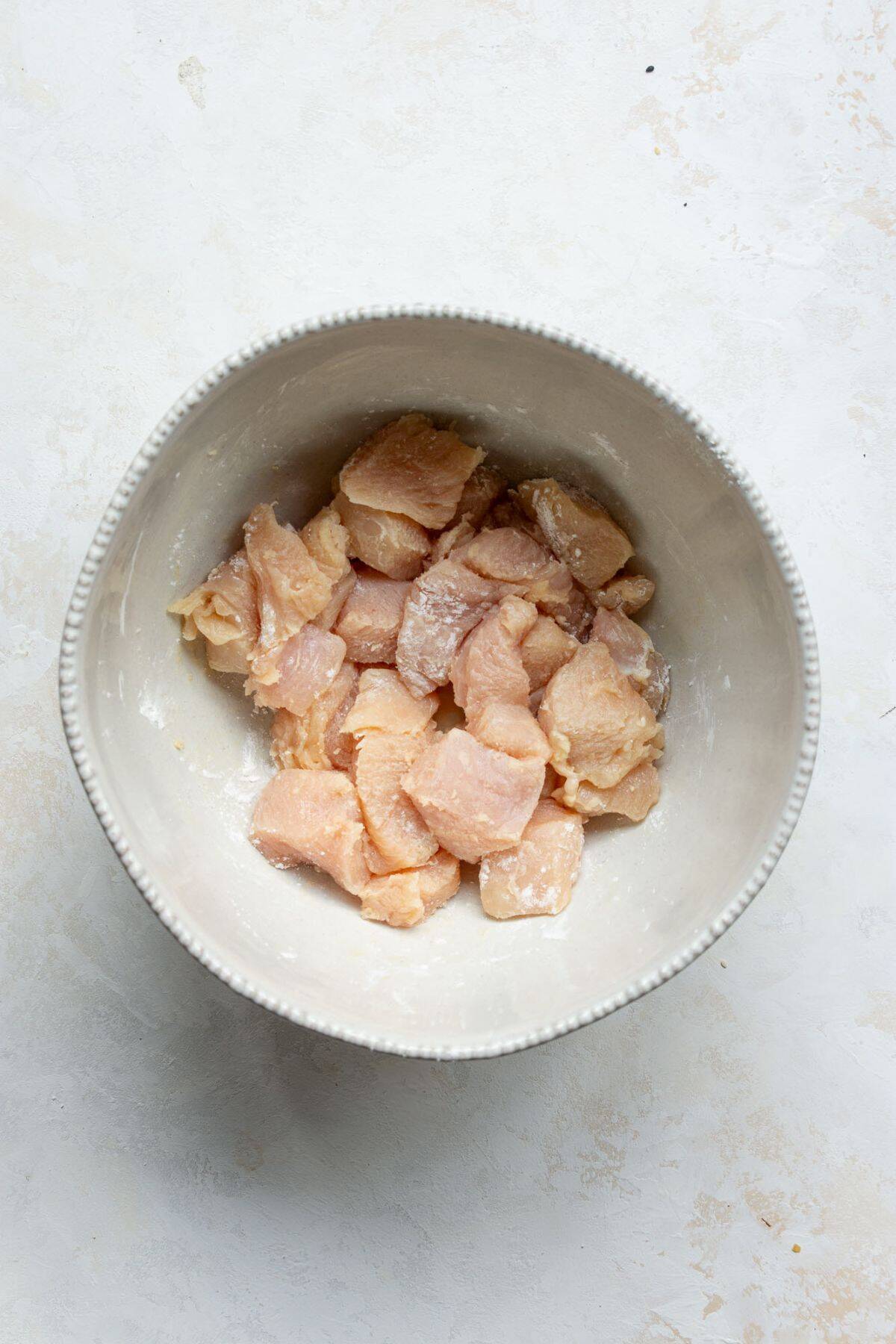 Bite-sized chicken breast pieces in a bowl coated with arrowroot starch before air frying.