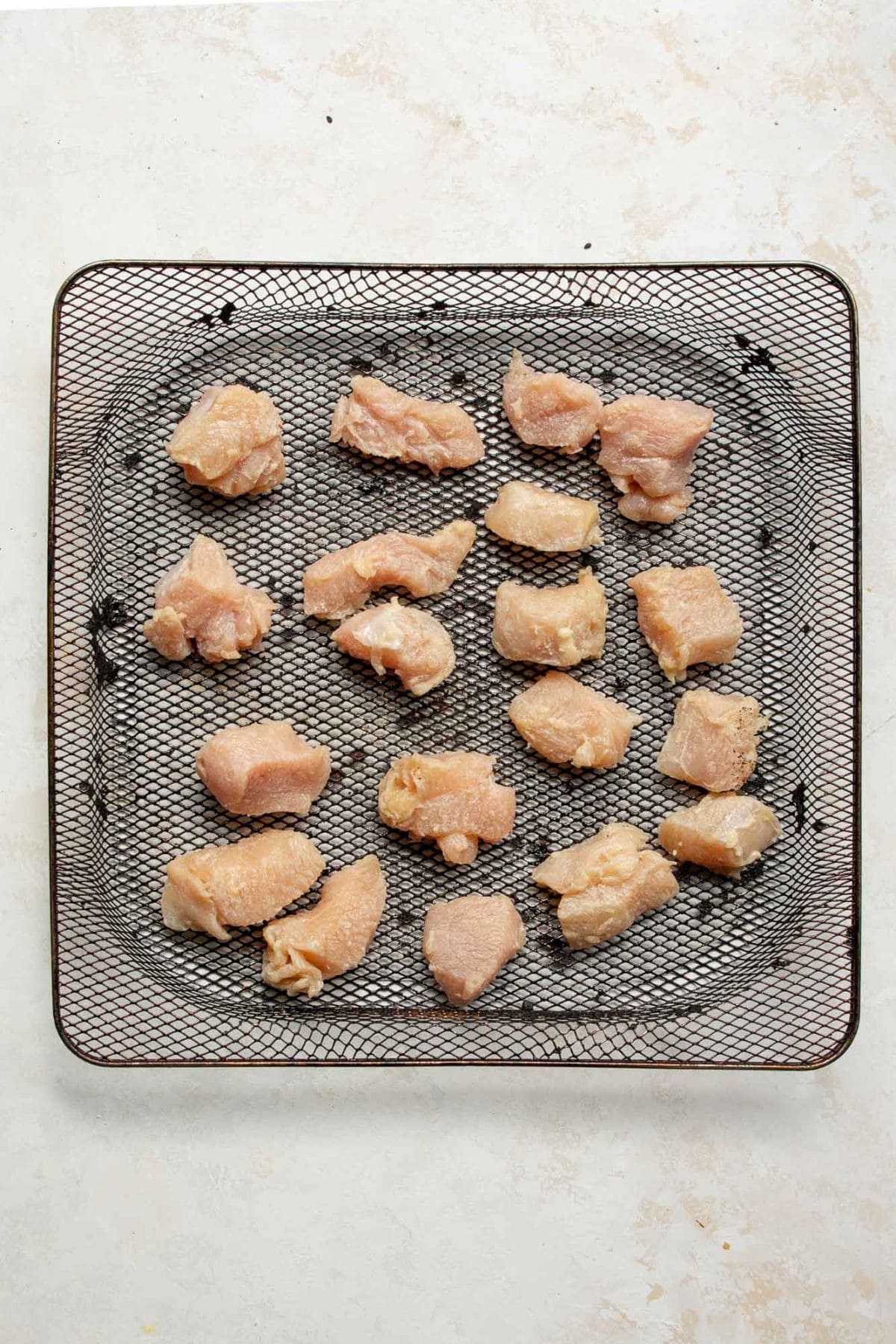 Raw chicken breast bites arranged in an air fryer basket before cooking.