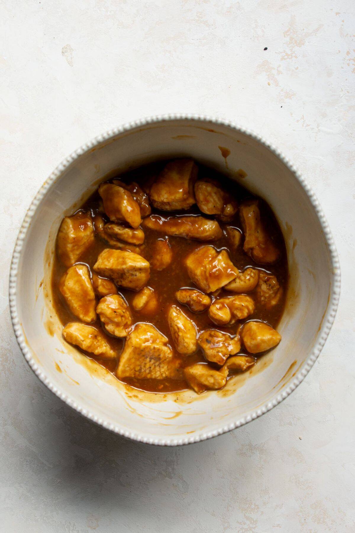 Crispy chicken pieces tossed in homemade teriyaki sauce in a mixing bowl.
