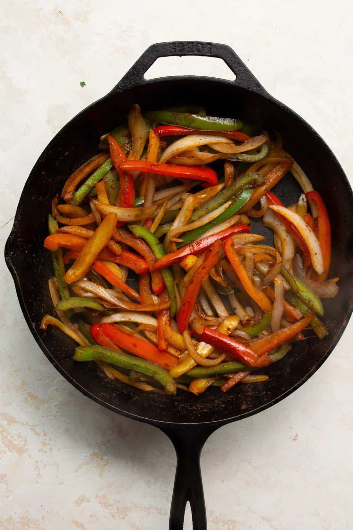 cooking bell peppers and onions in fajita seasoning in a cast iron pan