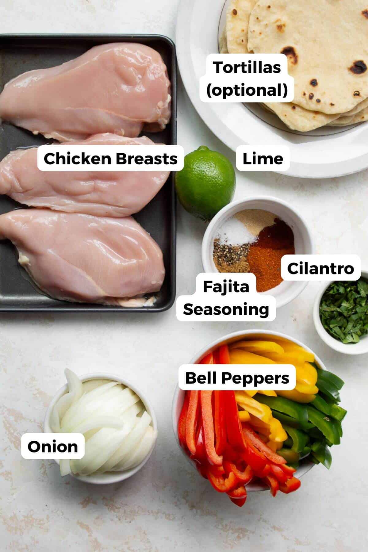 All ingredients in healthy chicken fajita skillet labeled, including: chicken breast, lime, fajita seasoning, cilantro, bell peppers, onion, and tortillas.