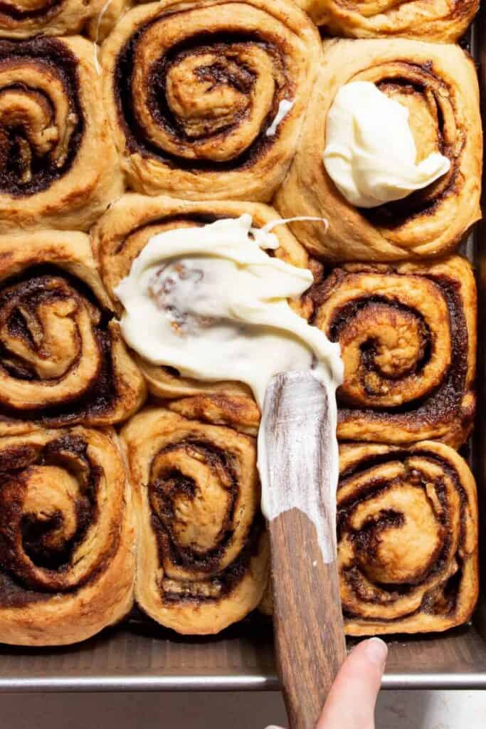 spreading cream cheese icing on banana bread cinnamon rolls