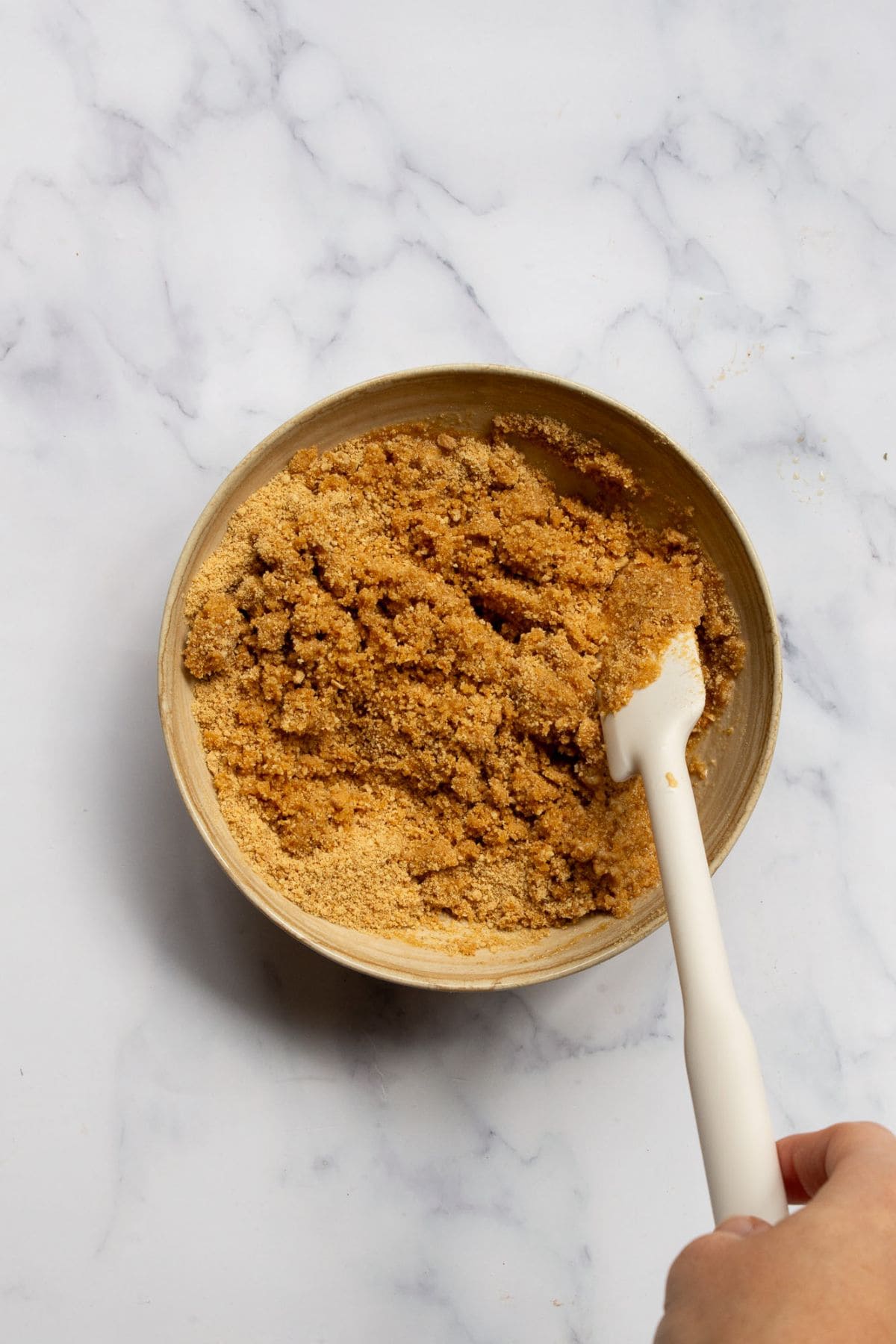 Gluten-free graham cracker crumbs and melted butter being mixed together in a bowl to form the crust.
