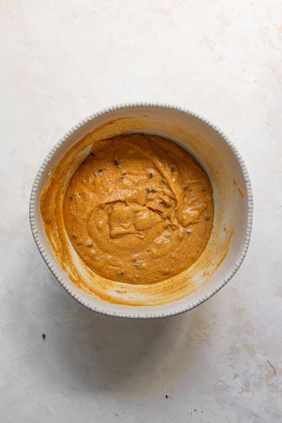 Protein powder, almond flour, and chocolate chips being added to the pumpkin muffin batter in a mixing bowl.