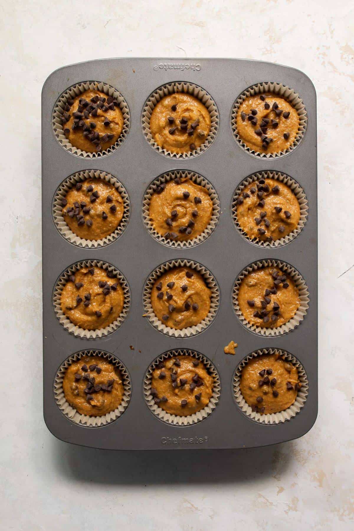 Unbaked pumpkin protein muffin batter divided into a cupcake tin, topped with chocolate chips before baking.