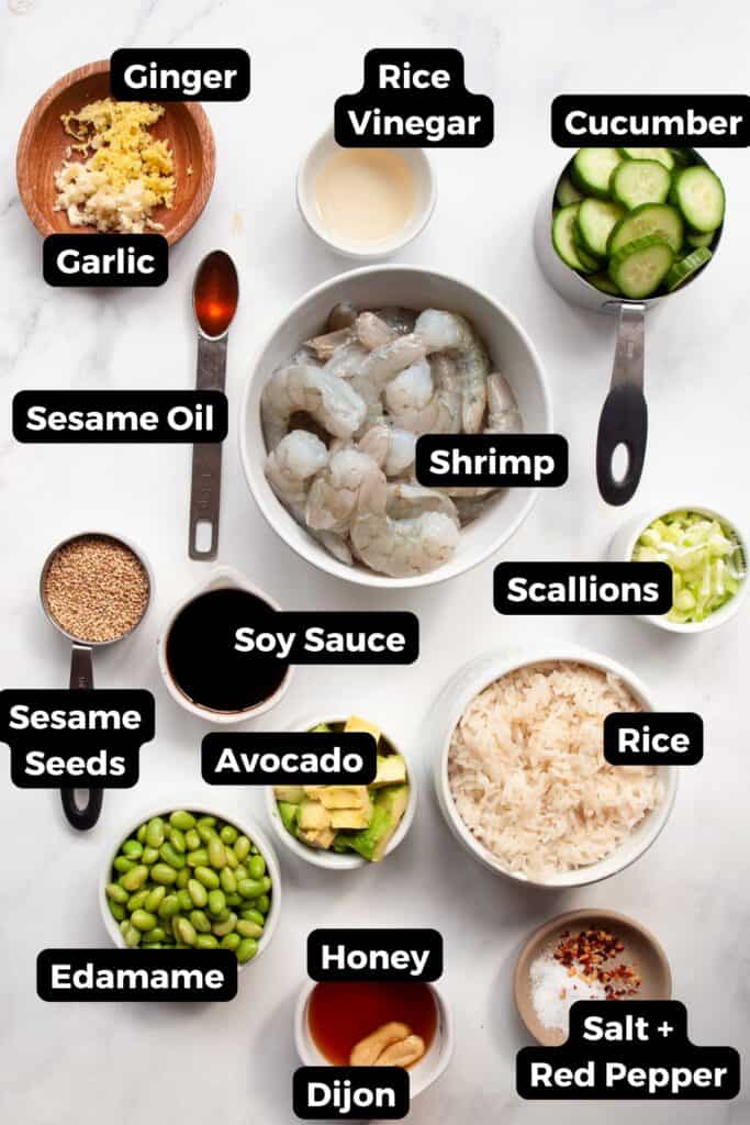 All ingredients for shrimp poke bowl displayed in small labeled bowls, including shrimp, pineapple, brown rice, pickled cucumber, edamame, honey soy dressing, and seasonings