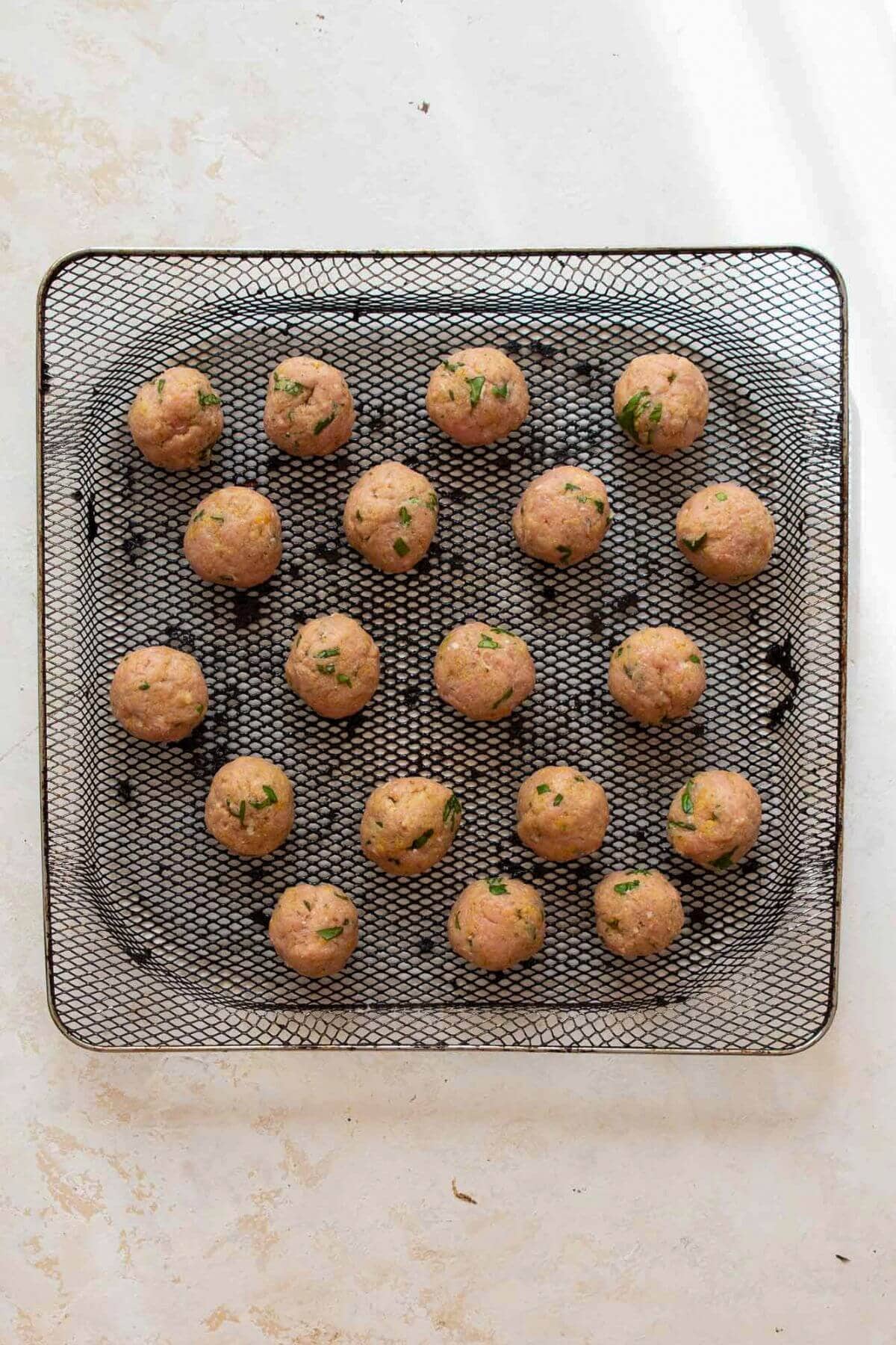 Raw turkey meatballs in air fryer basket before cooking.