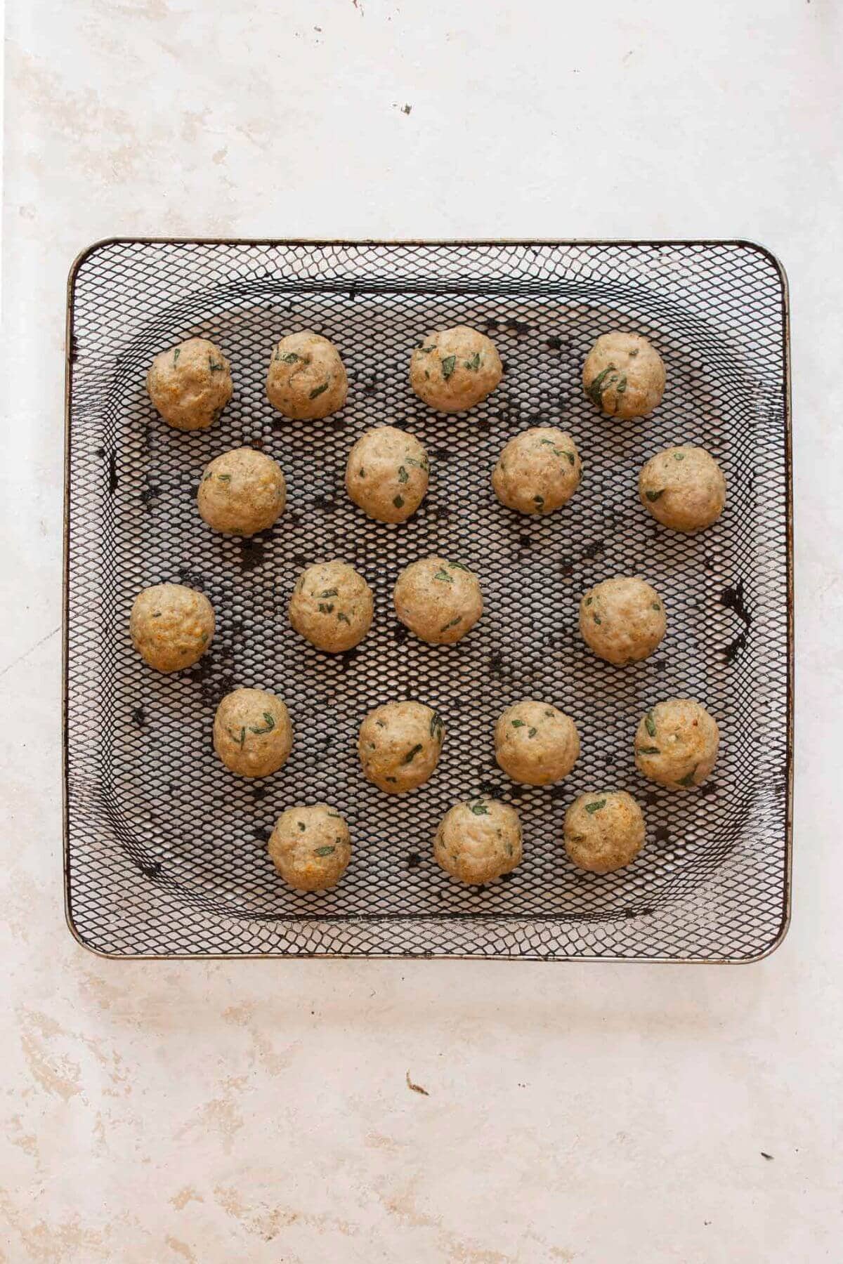 Cooked crispy and juicy turkey meatballs in air fryer basket.
